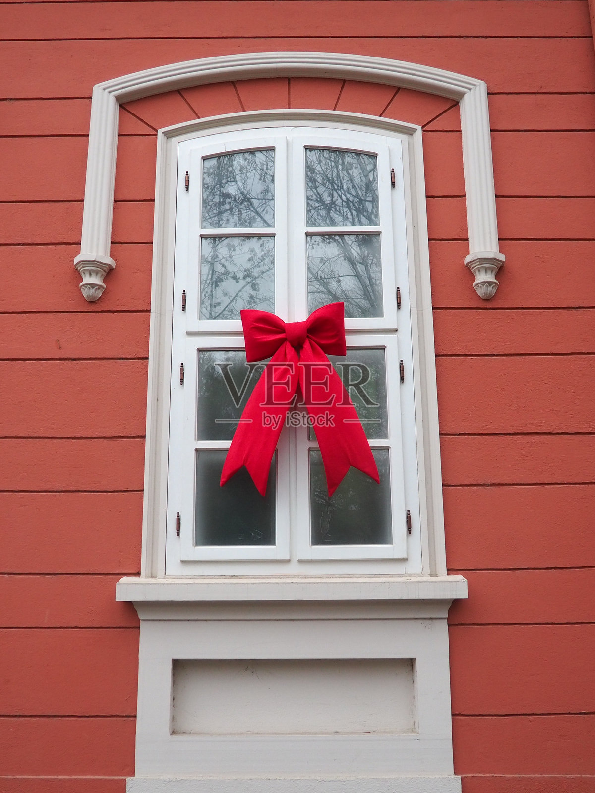 一个迷人的窗户装饰着新年和圣诞节的装饰,展示了一个大红色蝴蝶结,为冬季节日或聚会营造了欢乐的氛围。照片摄影图片