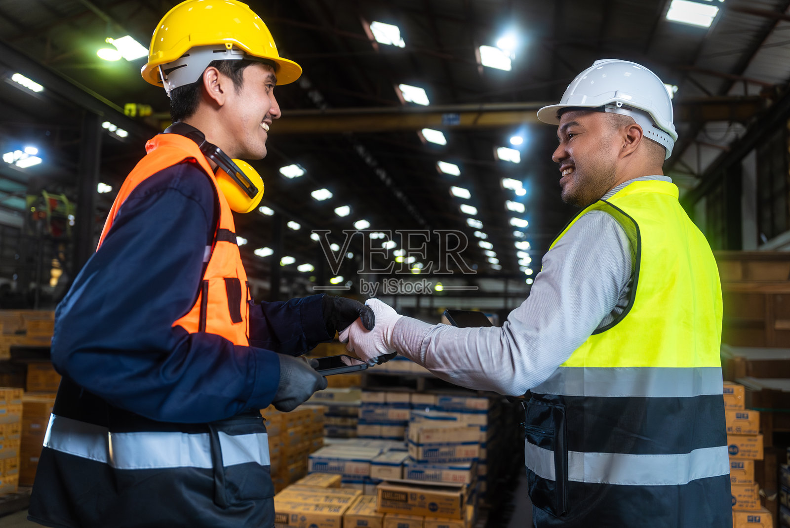 专业工程师和技术人员戴着安全头盔,在工厂仓库中使用平板电脑进行分析会议。自信的工厂工人团队正在检查工业工厂。团队合作概念。照片摄影图片