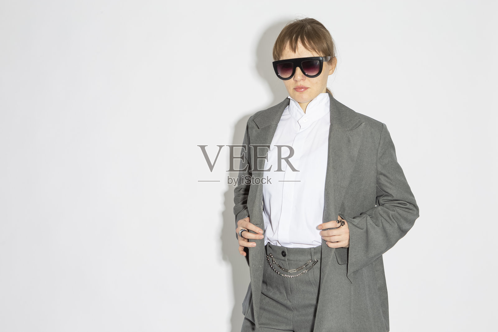 穿着灰色西装的女商人全身肖像,戴着深色眼镜,背景为白色。照片摄影图片