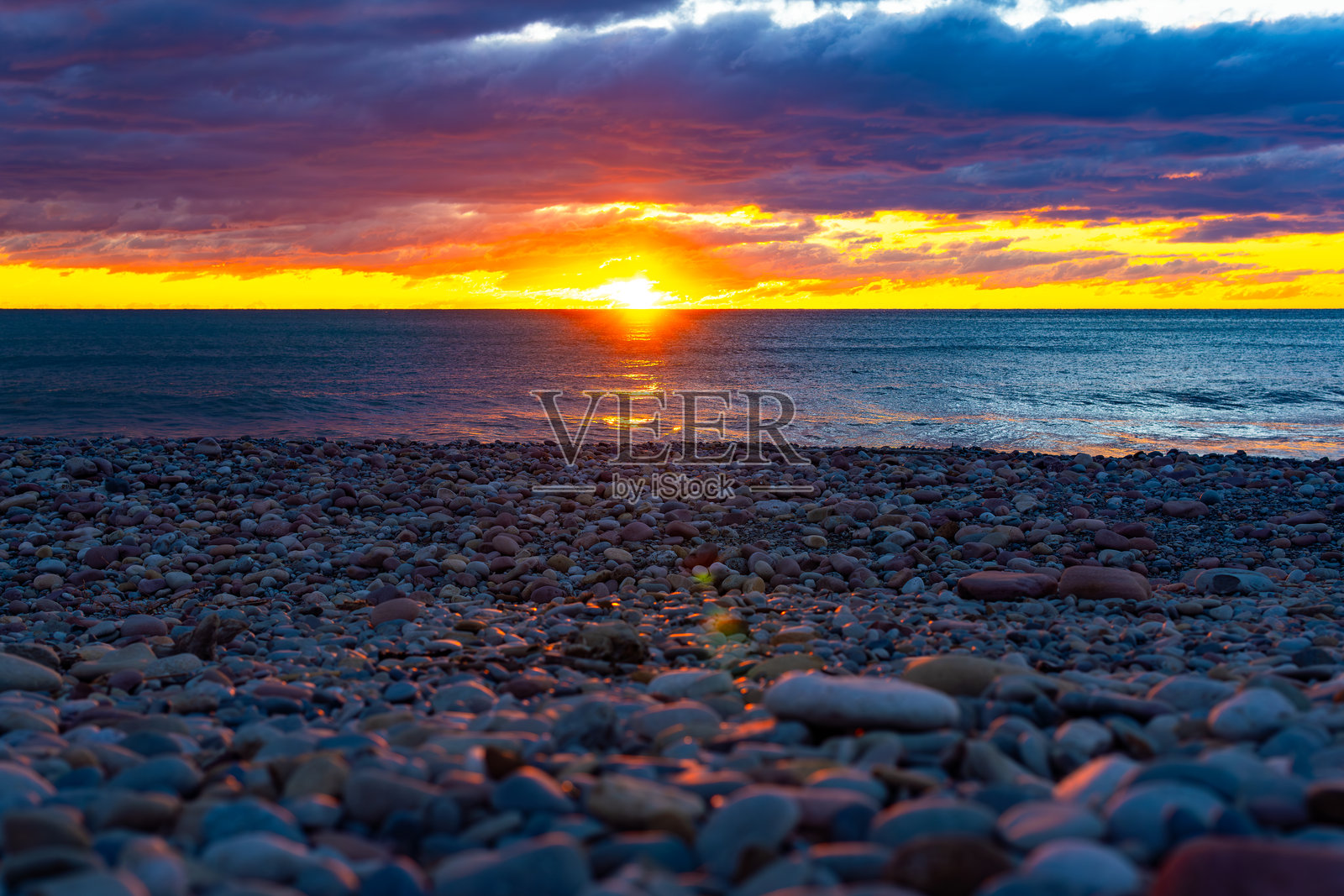 日出时分,金色、紫色和橙色的多云天空映衬着海岸线的卵石沙滩,俯瞰着壮丽而美丽的地平线。概念:宁静的风景,平和与安宁,重要的反思。照片摄影图片