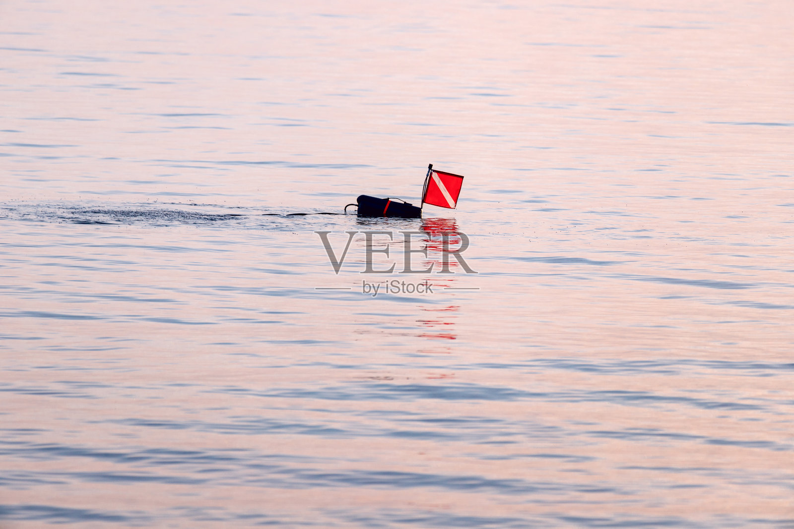 潜水旗漂浮在宁静的水面上,标志着日落时水下探险的存在。照片摄影图片
