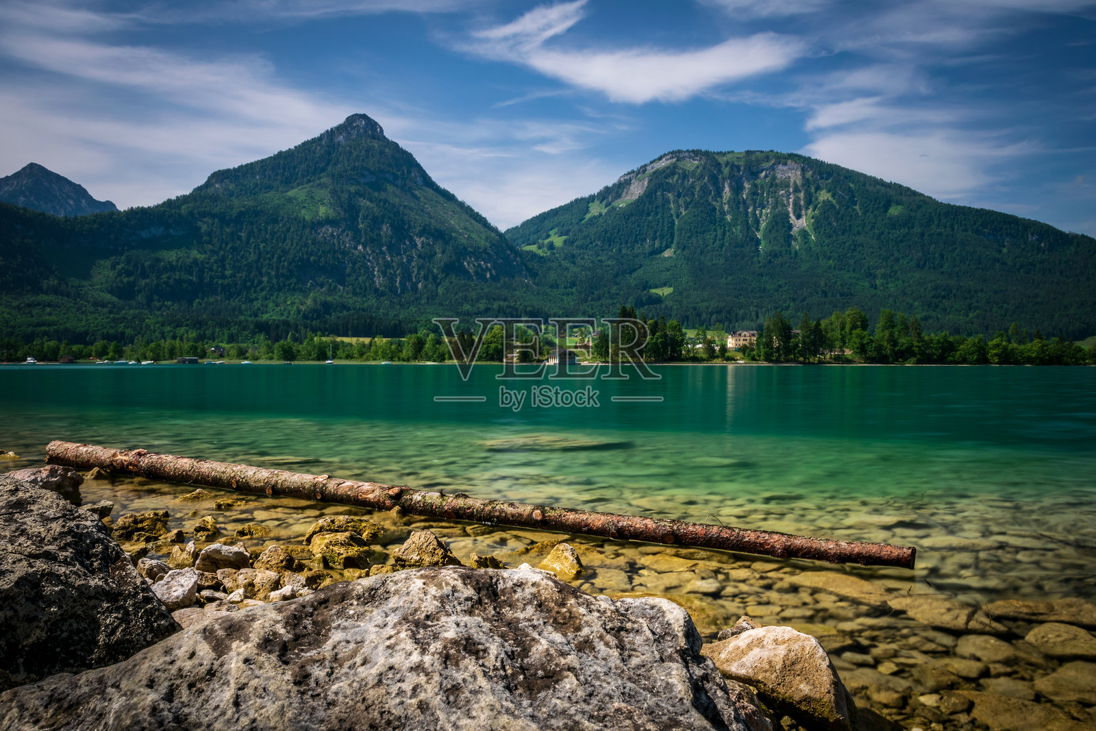 奥地利沃尔夫冈湖前的岩石,清澈的湖水呈现出蓝绿色,背景是山脉和天空中的云朵。照片摄影图片