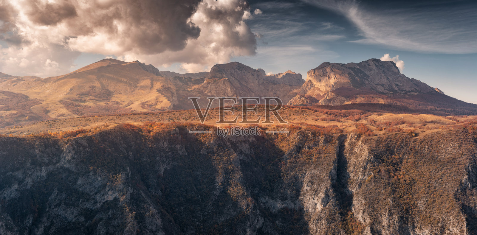 金色时光的阳光照耀着壮丽的山脉和峡谷,秋天的色彩在戏剧性的云层下显得格外迷人。照片摄影图片