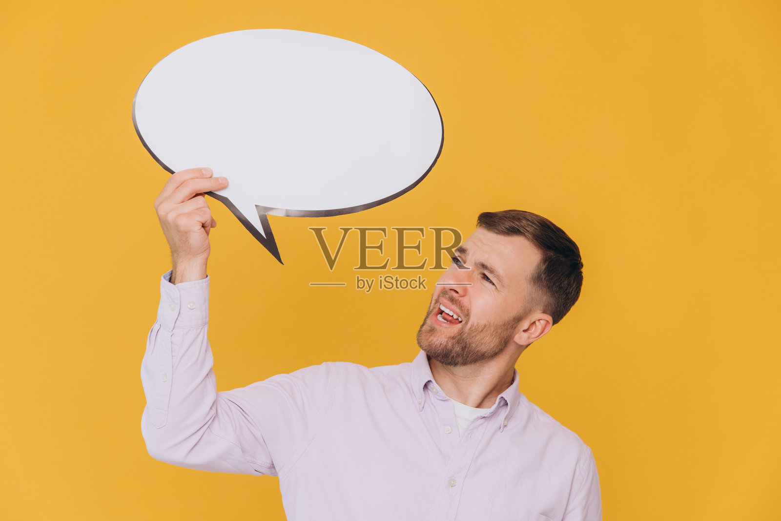 可爱的未剃须男士手持空白云朵,演讲气泡宣传内容,背景为黄色工作室肖像。照片摄影图片