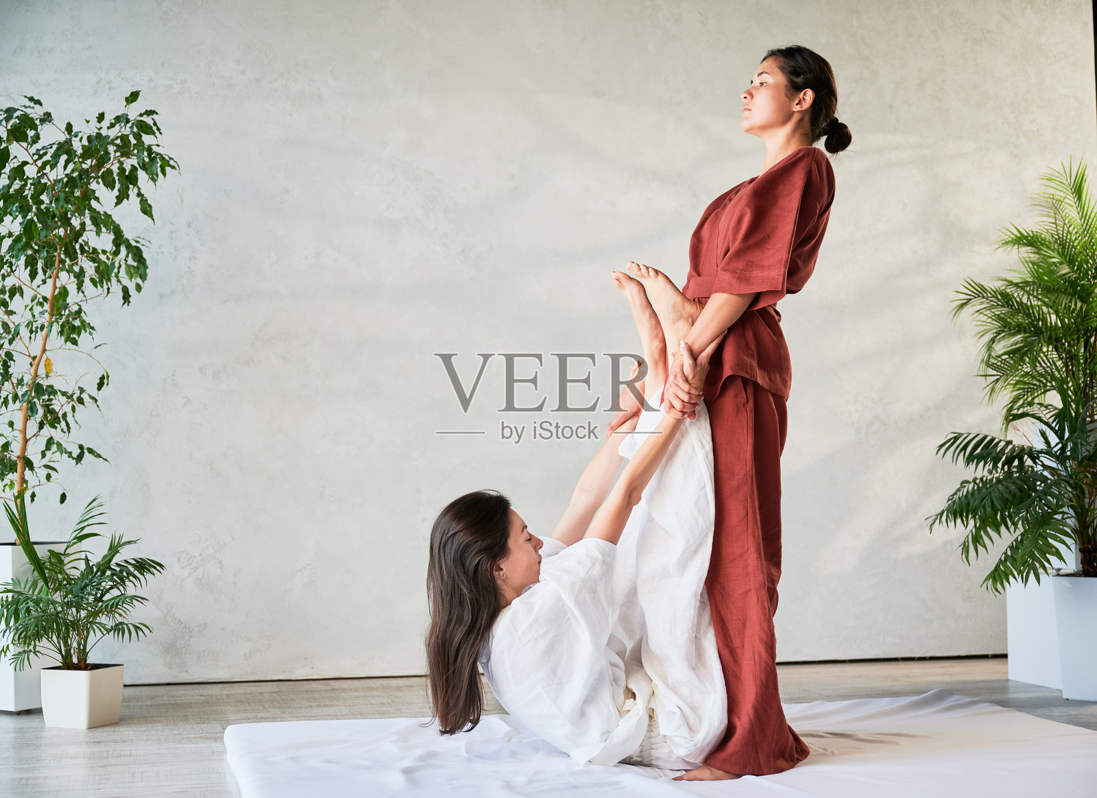 按摩师为女性患者进行泰式瑜伽按摩,拉伸她的身体。照片摄影图片