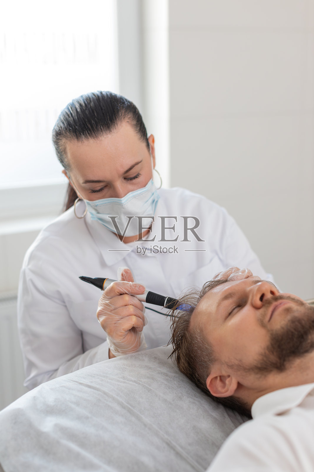 毛发专家为男性进行改善头发生长的治疗,包括微针美容仪和维生素注射。照片摄影图片