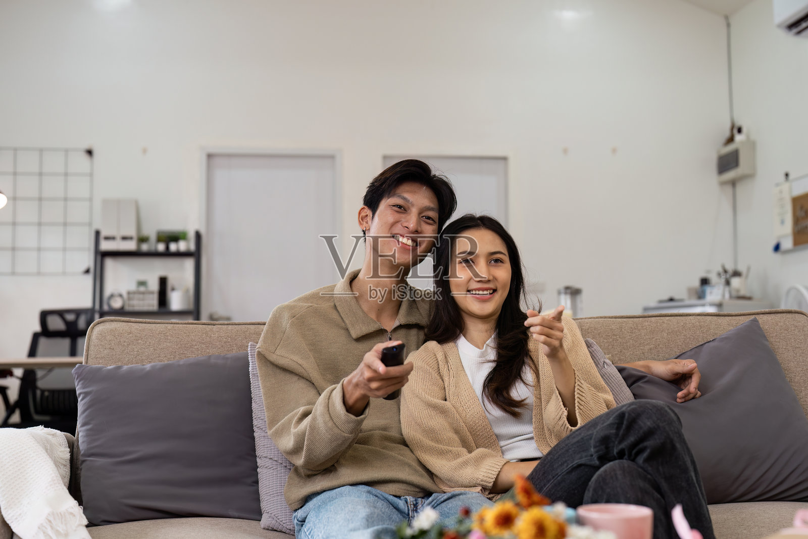 幸福的情侣在现代客厅的沙发上放松,观看电视,周围有舒适的装饰和温暖的灯光。照片摄影图片