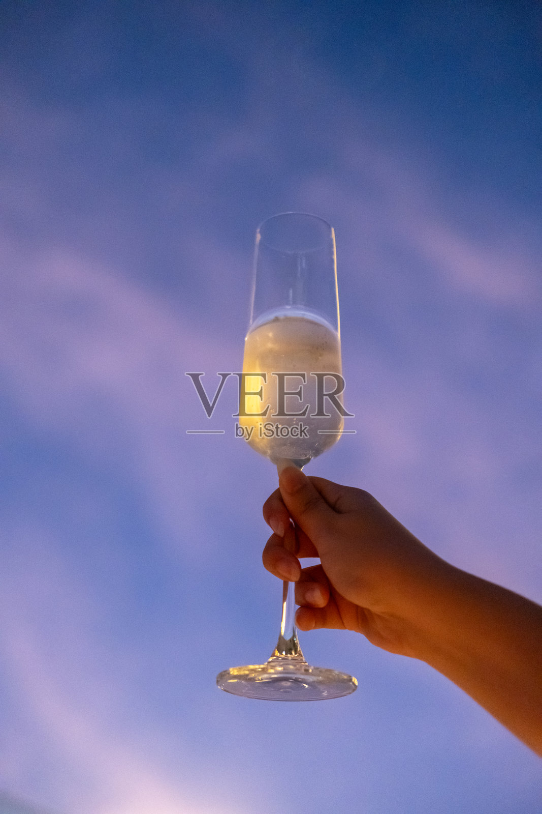 一只手握着一杯普罗塞克或起泡酒,背景是五彩斑斓的日落天空照片摄影图片