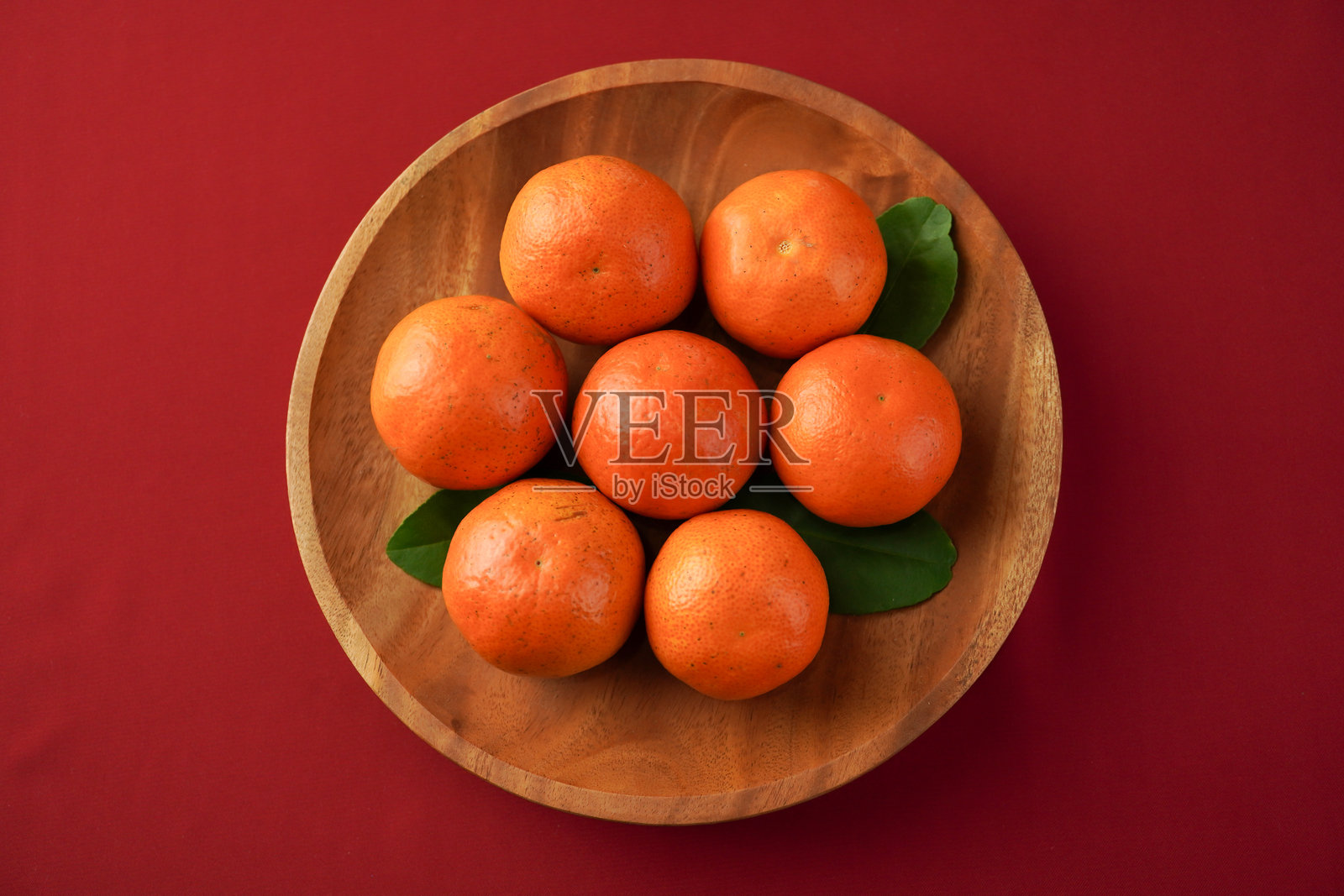 成熟的橙子放在木盘上,摆放在红色桌布的桌子上。背景为红色。春节概念照片摄影图片