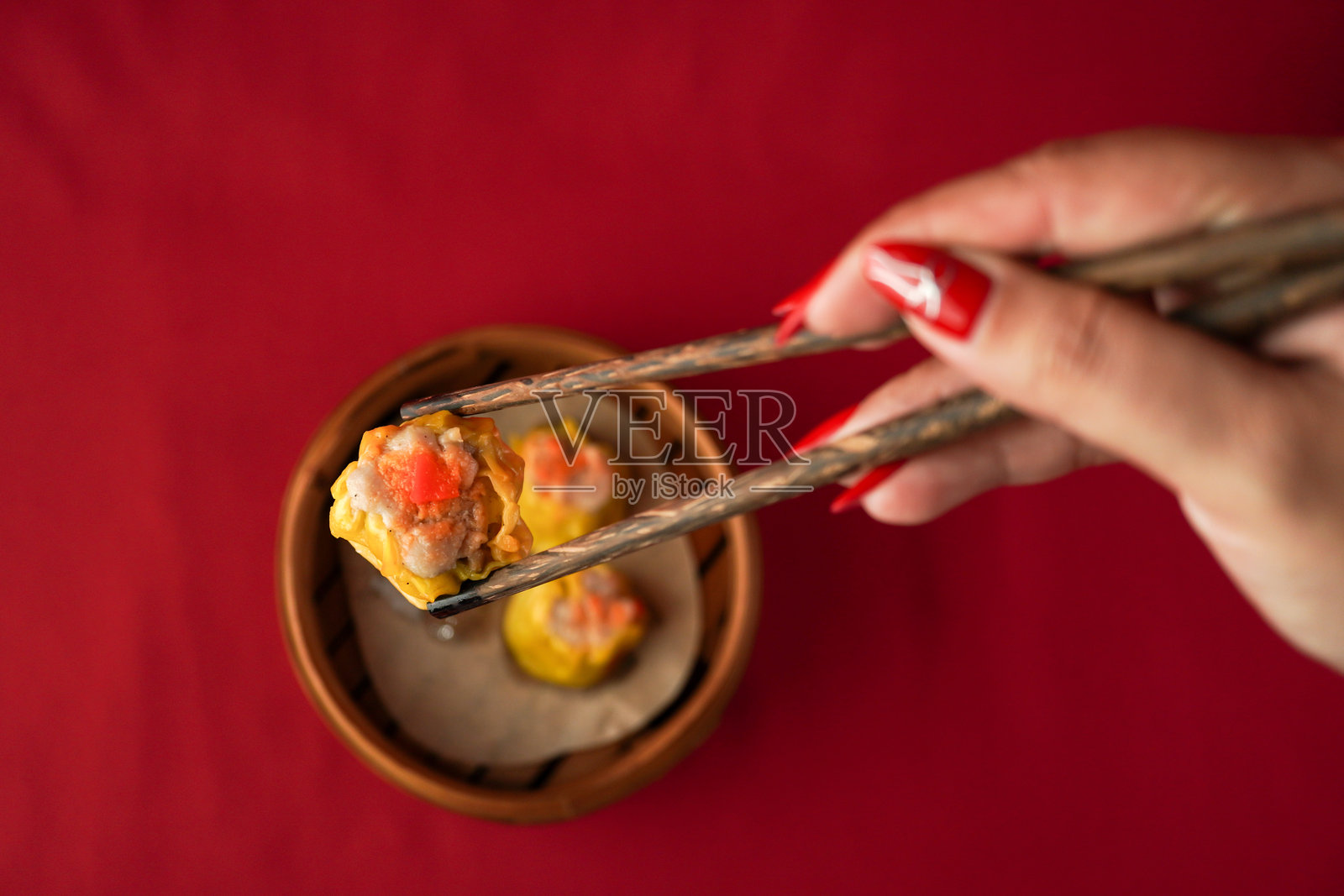 亚洲女性用木筷子夹取点心。蒸饺子适合春节派对,背景为红色。照片摄影图片