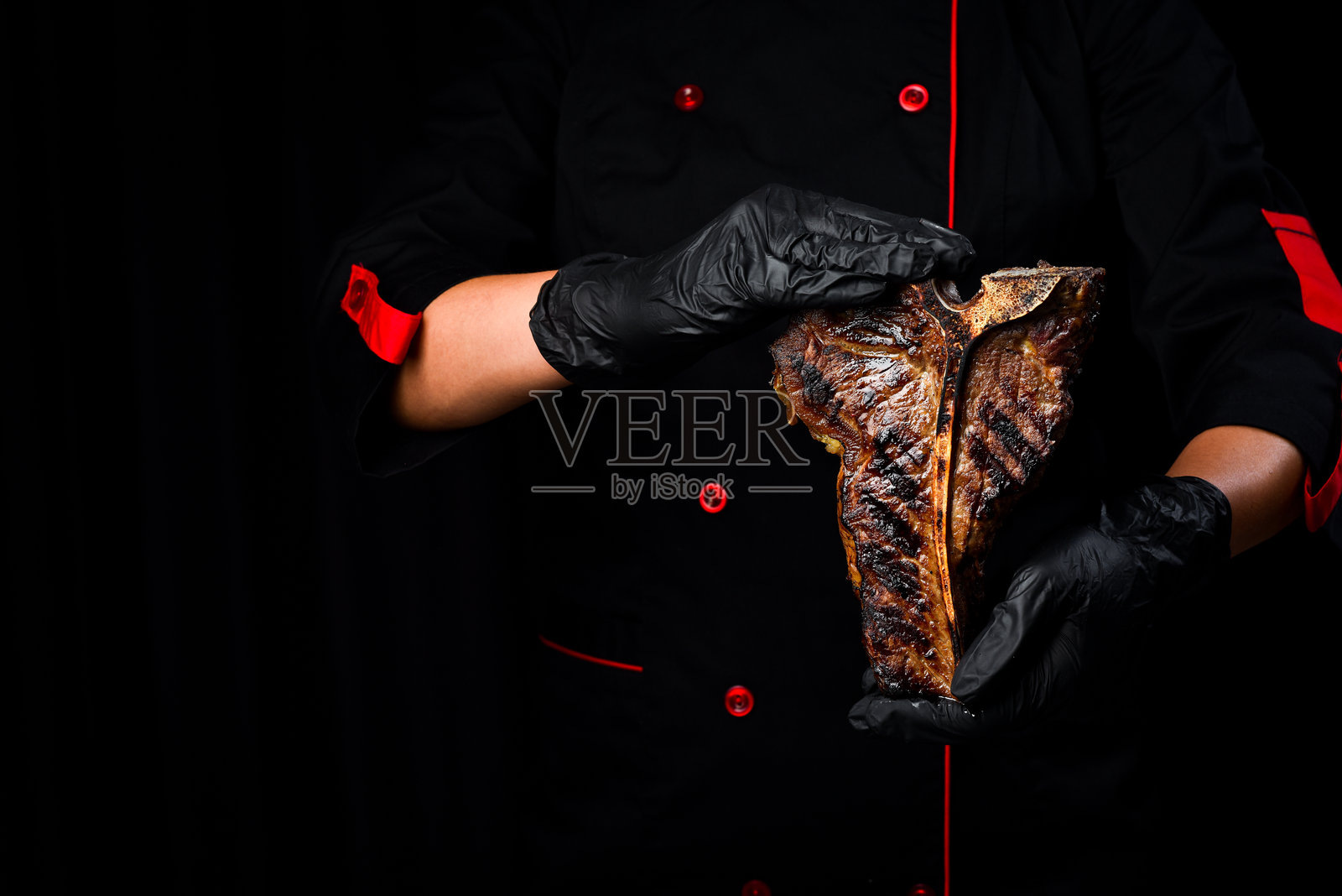 厨师手中拿着带骨牛排。优质黑安格斯T骨牛排。特写。黑色背景。照片摄影图片