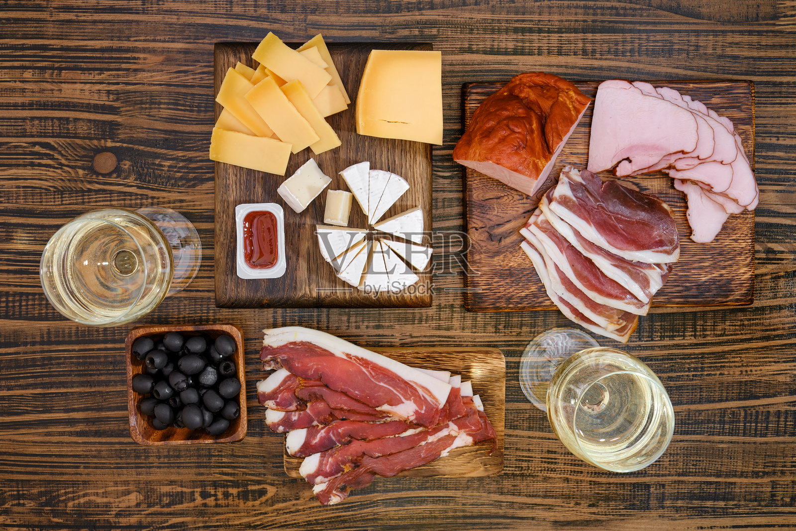 从上方俯视木桌上的肉类和奶酪拼盘,旁边有葡萄酒和橄榄。照片摄影图片