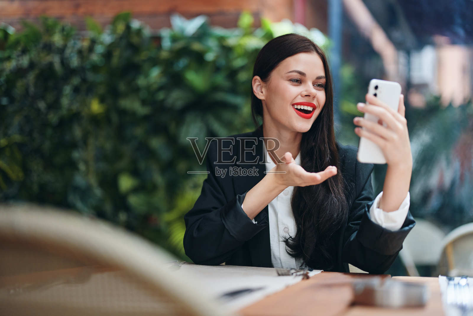 时尚女性博主游客坐在咖啡馆里,手中拿着手机阅读信息,旅途中的移动通信和互联网,视频通话,在线自由职业,露出微笑。照片摄影图片