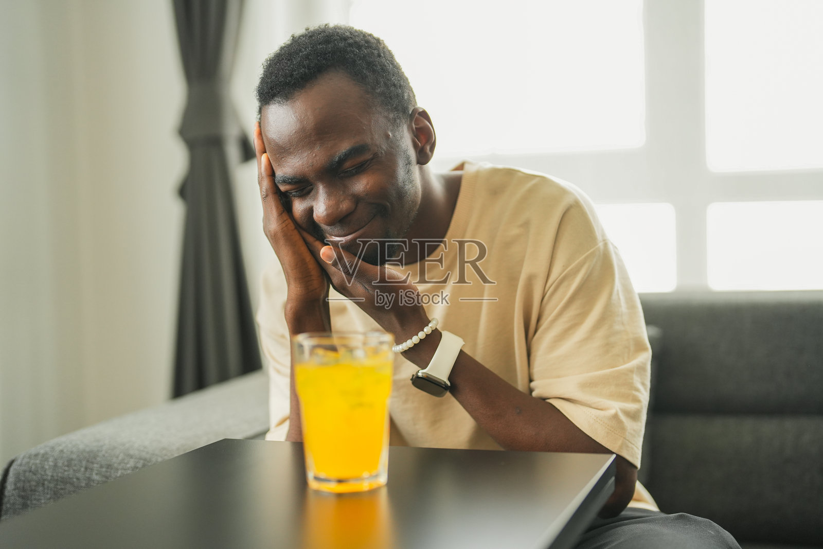 一位牙齿敏感的黑人男性在家中沙发上喝冰饮料照片摄影图片