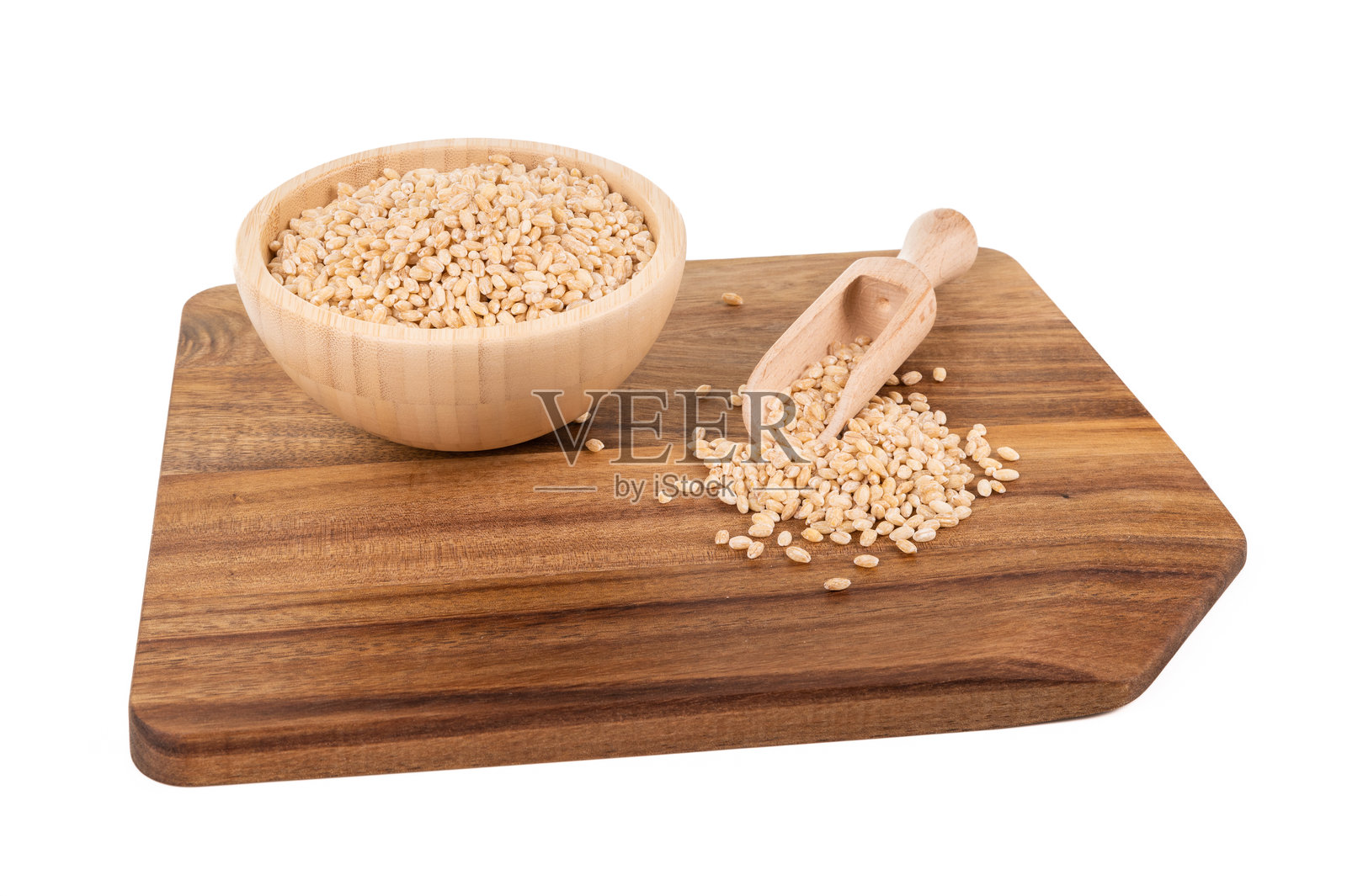 木碗中的珍珠大麦,旁边放着一个铲子,置于切菜板上照片摄影图片