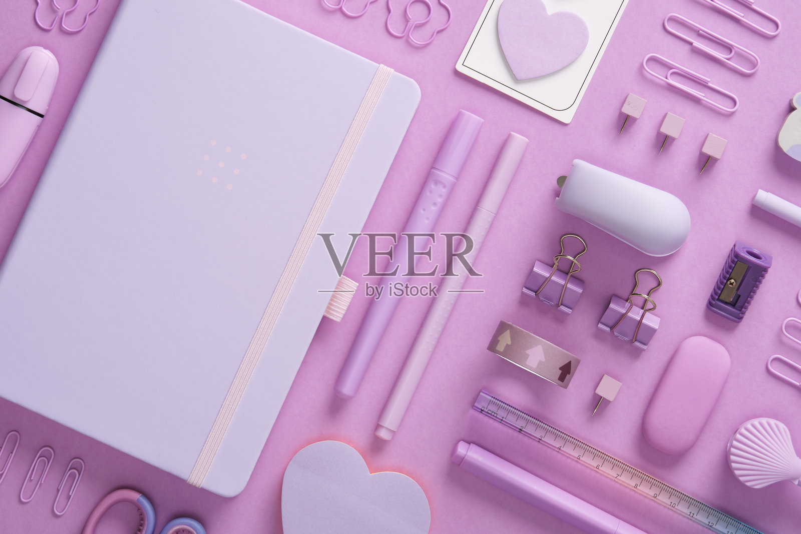 淡紫色文具背景,包括记事本、纸夹、剪刀、便签纸、彩色笔、橡皮擦、订书机、尺子和图钉照片摄影图片