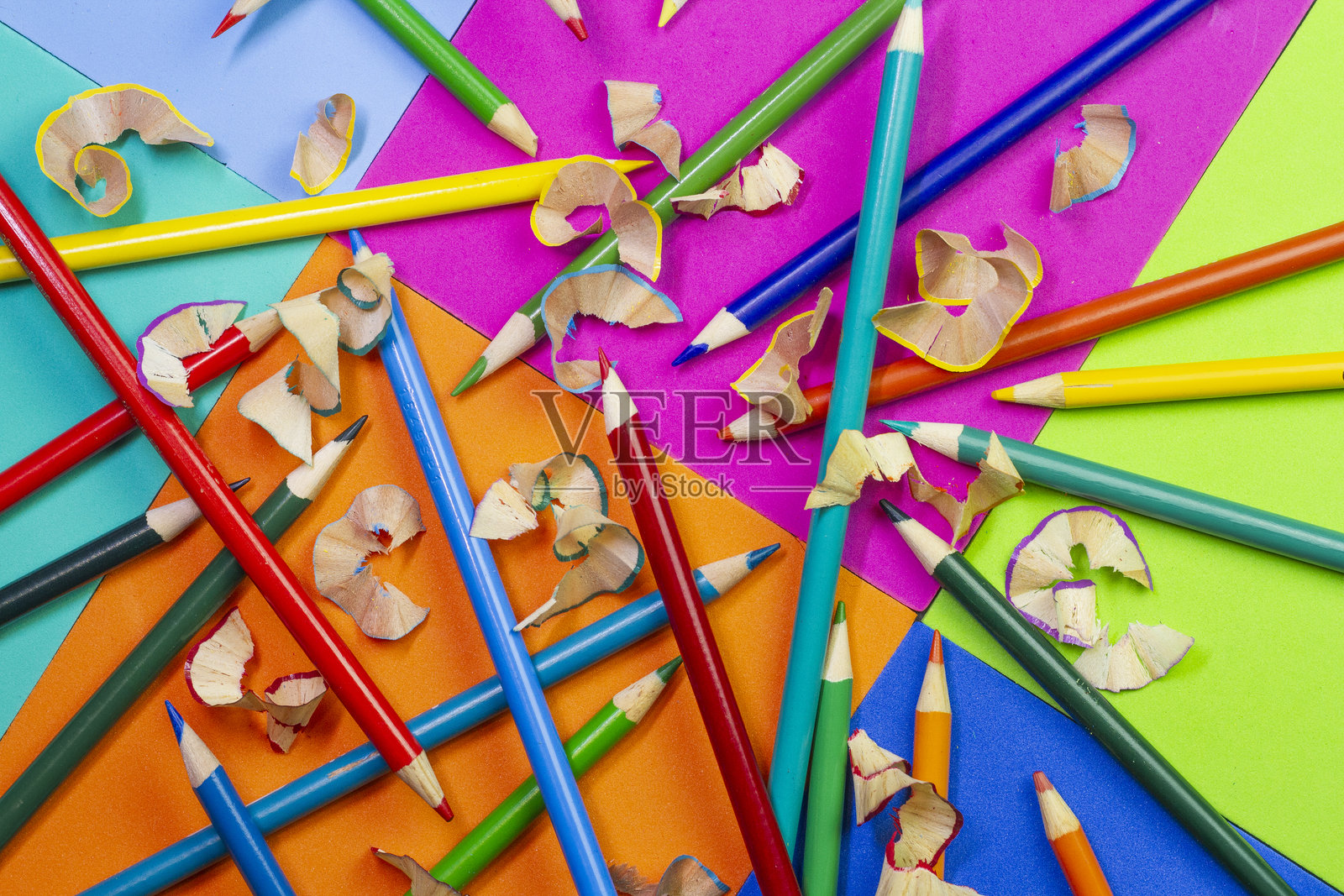 五彩铅笔和削好的铅笔屑在充满活力的几何纸背景上。照片摄影图片