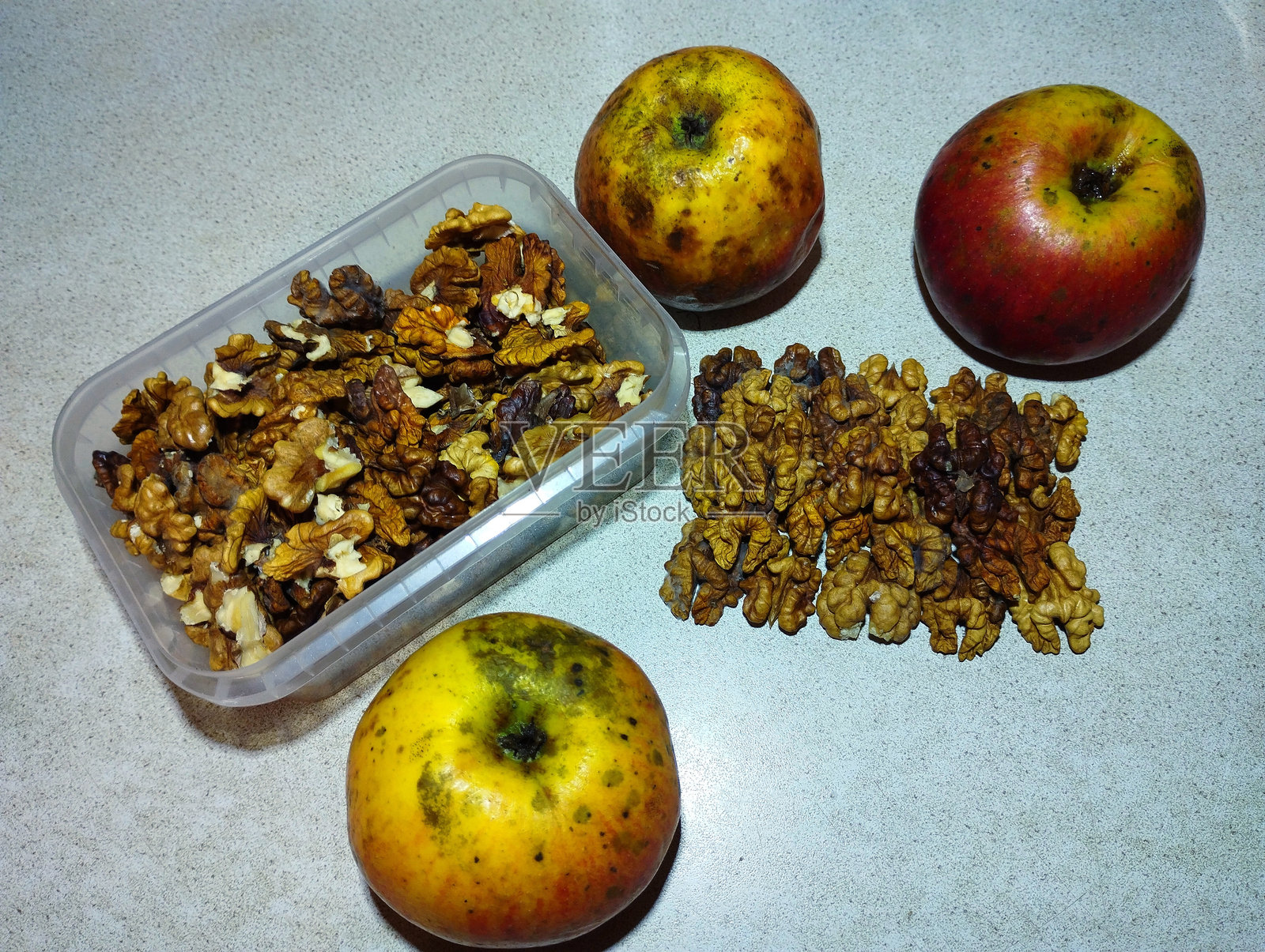 自制的苹果和剥皮的核桃放在厨房台面的灰色表面上。苹果和核桃的静物。照片摄影图片