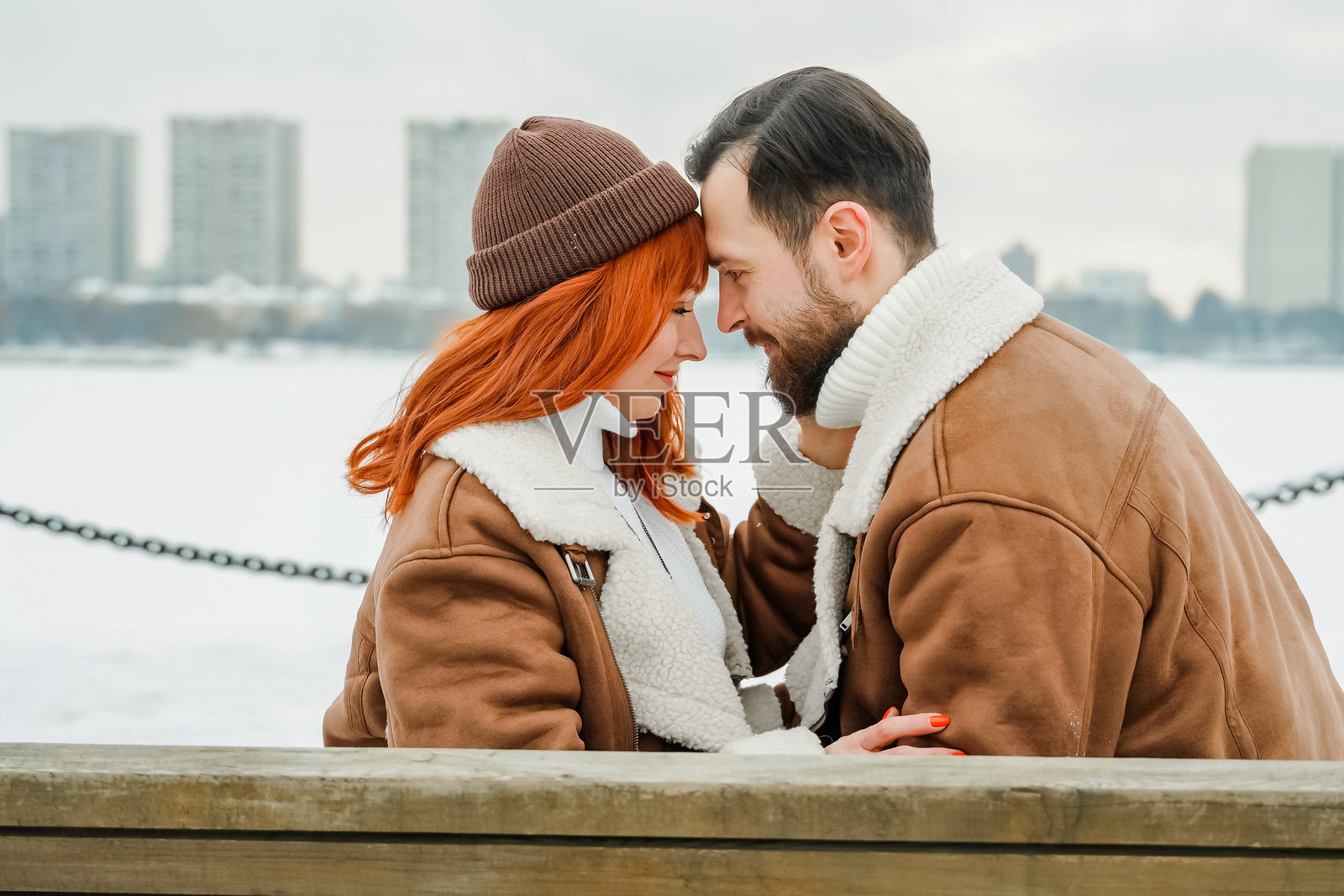 浪漫情侣爱情故事。粗犷的胡子男人,明亮的红发女孩在冬季公园。浪漫约会,亲吻,拥抱。散步,玩乐。时尚服装,红色羊皮大衣,夹克,帽子。照片摄影图片