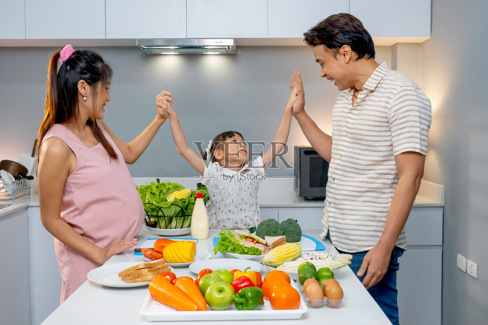 小女孩和父亲、怀孕的母亲在厨房里开心地手牵手准备做饭。照片摄影图片