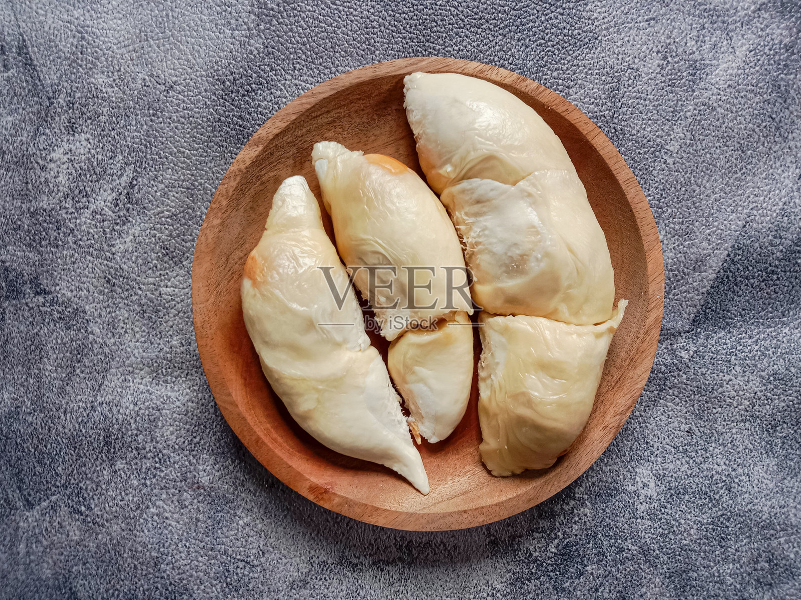 灰色背景上木盘中的榴莲果肉特写。木盘里的去皮榴莲果。俯视图。照片摄影图片