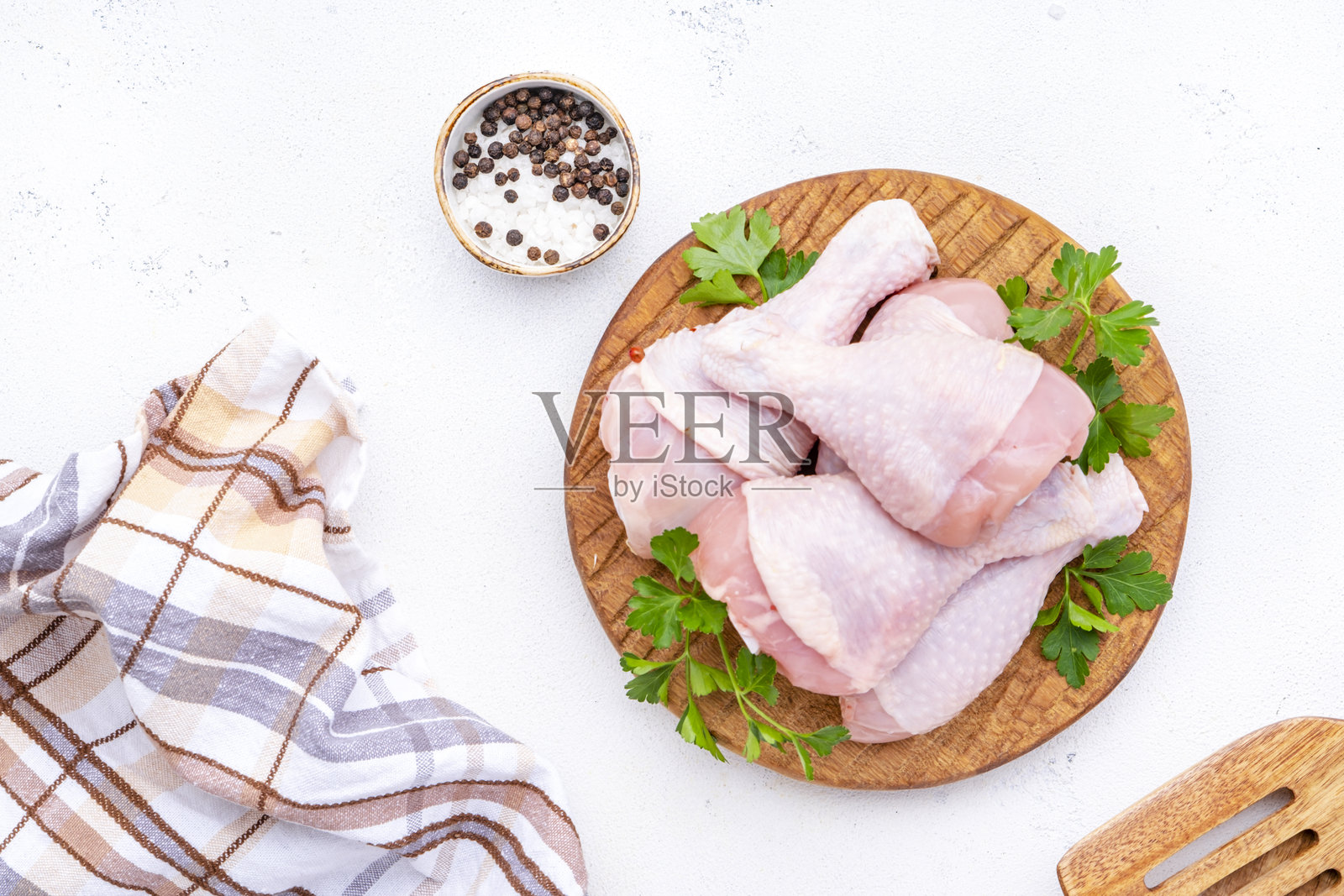 原木圆板上的生鸡腿,旁边有胡椒、盐和香 parsley。白色背景,俯视图。照片摄影图片