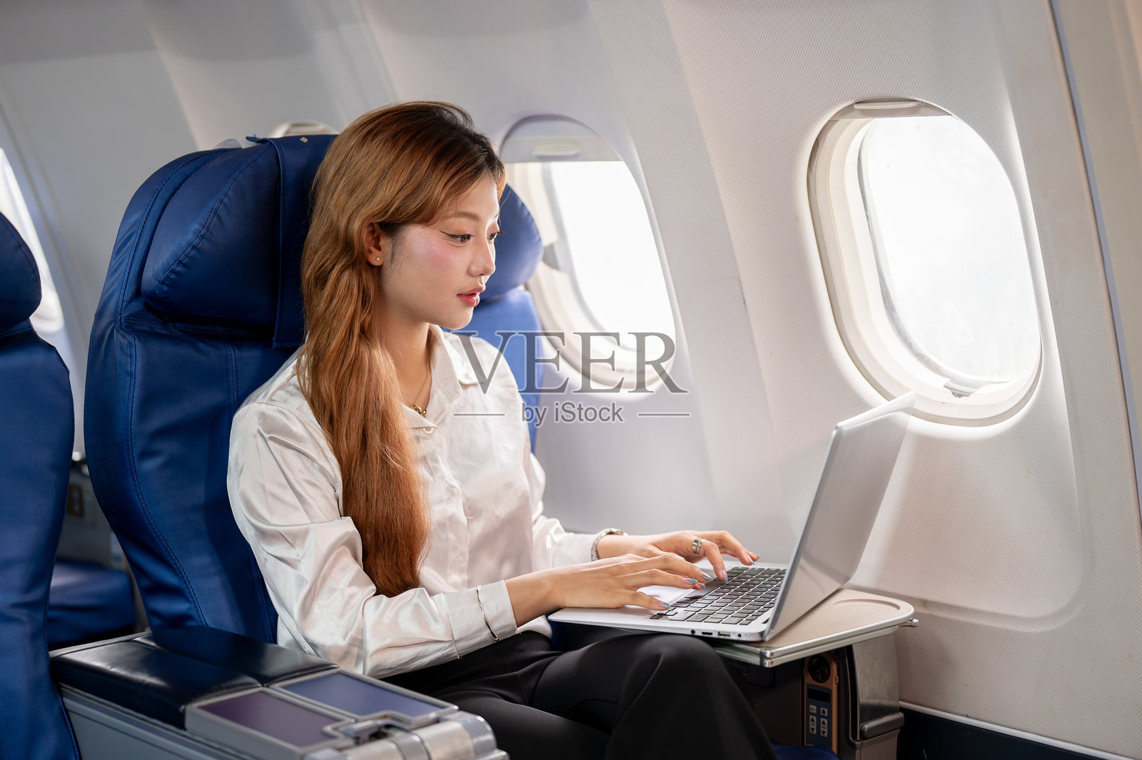 一位迷人的亚洲女商人在飞往商务旅行的航班上使用笔记本电脑。照片摄影图片