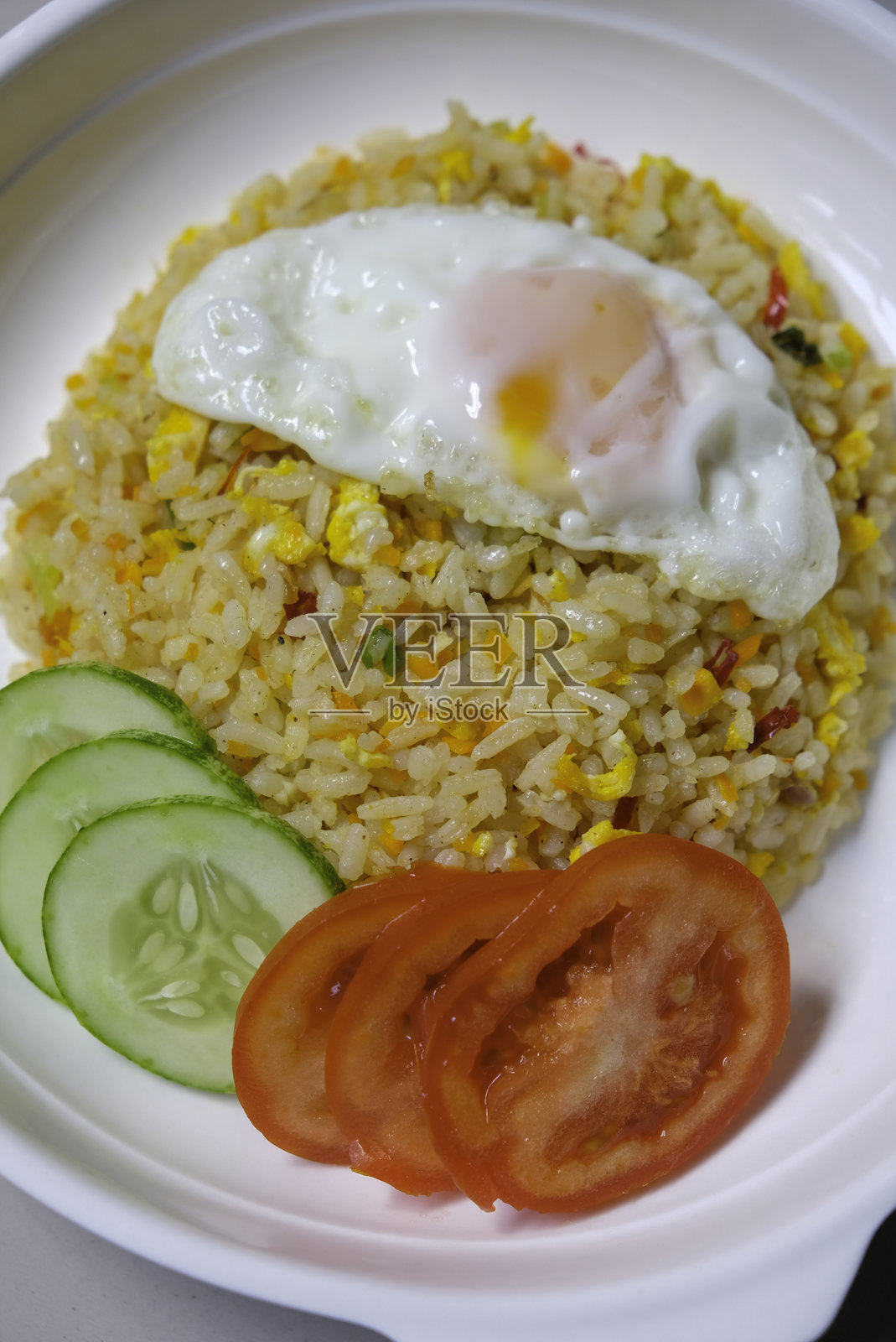 印尼炒饭,配有煎蛋、番茄和黄瓜,盛在白色盘子里。照片摄影图片