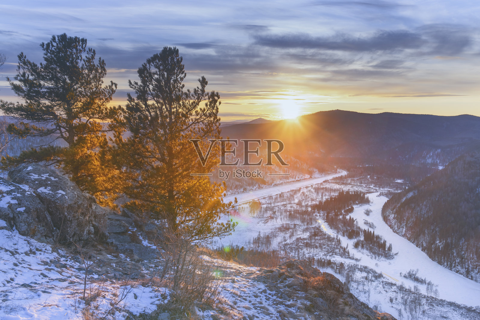 壮观的冬季日落照亮了一个雪覆盖的山谷,河流优雅地蜿蜒其中。照片摄影图片