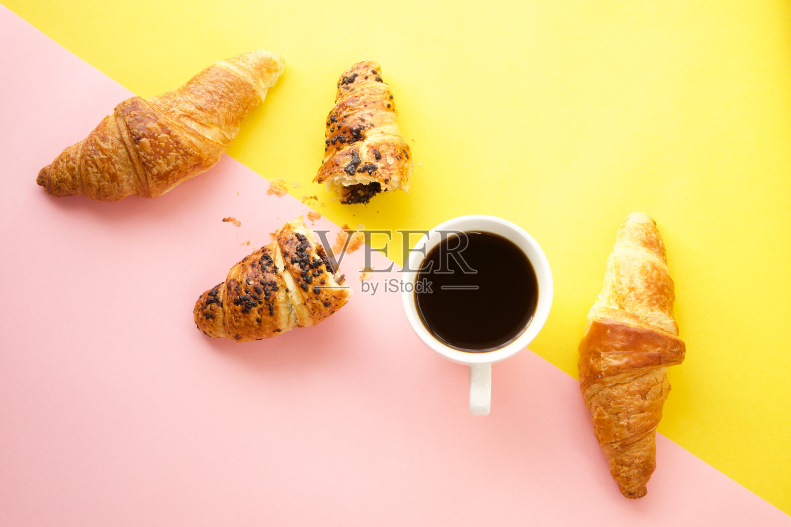 咖啡杯和新鲜的可颂面包在黄色和粉色背景上照片摄影图片