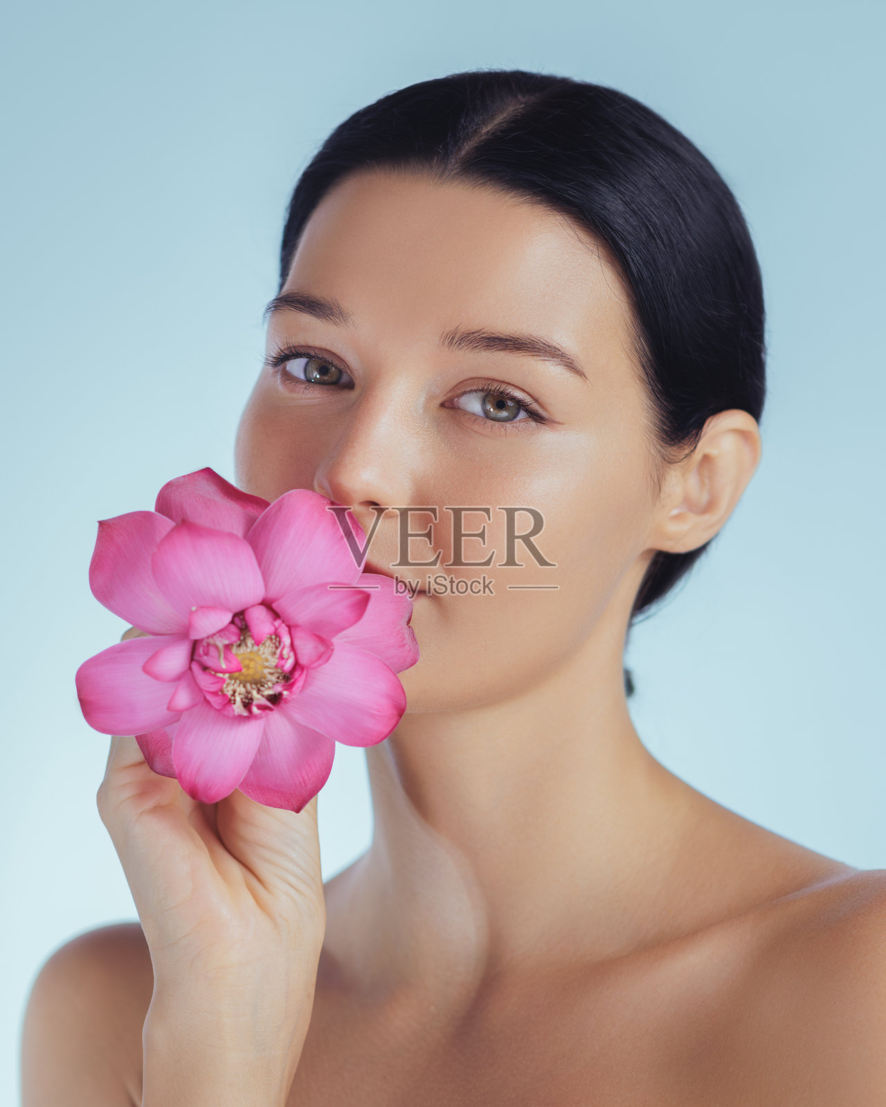 宁静的女性手持粉色莲花,代表自然护肤和美容理念照片摄影图片