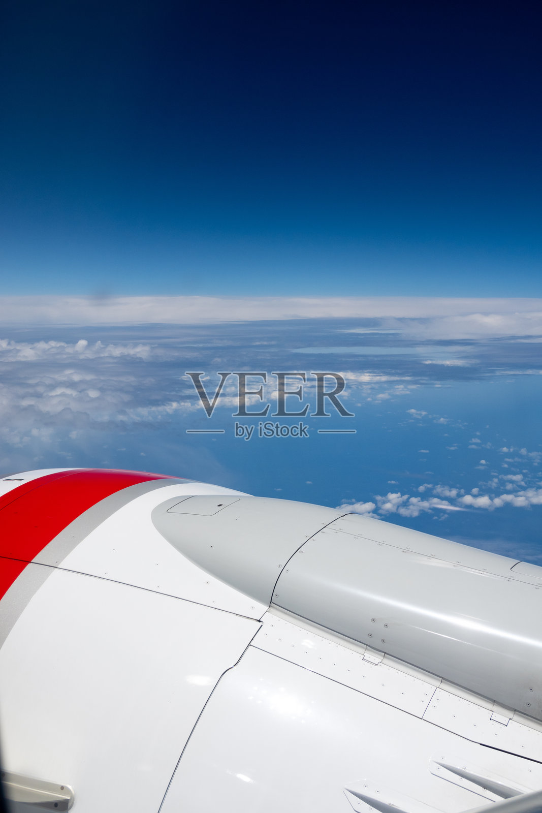 高空视角展现了黑暗的太空天空,下面是白色蓬松的云朵,前景中是飞机的机翼和引擎。照片摄影图片