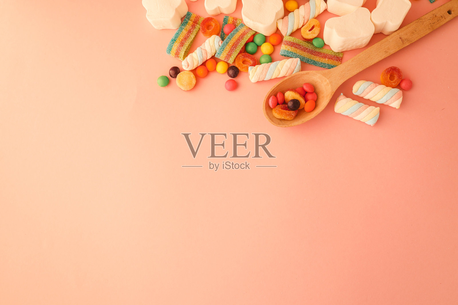 多种不同的果冻糖果和棒棒糖在粉色背景上,平铺展示。留有文字空间。照片摄影图片