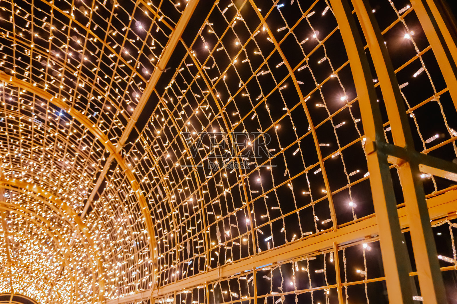 光的抽象:金色的发光隧道背景中,数不清的小灯光交织成网格状,令人联想到圣诞前夜和新年庆祝活动中装饰城市的花环。照片摄影图片