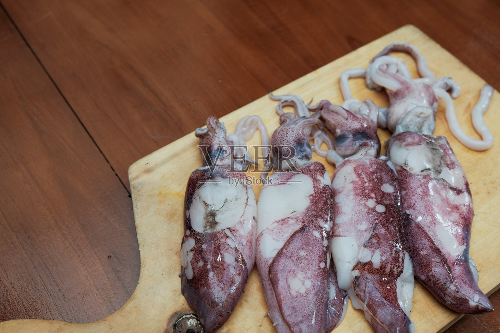 新鲜生鱿鱼放在木砧板上,背景是海鲜鱿鱼,准备切割和烹饪。照片摄影图片