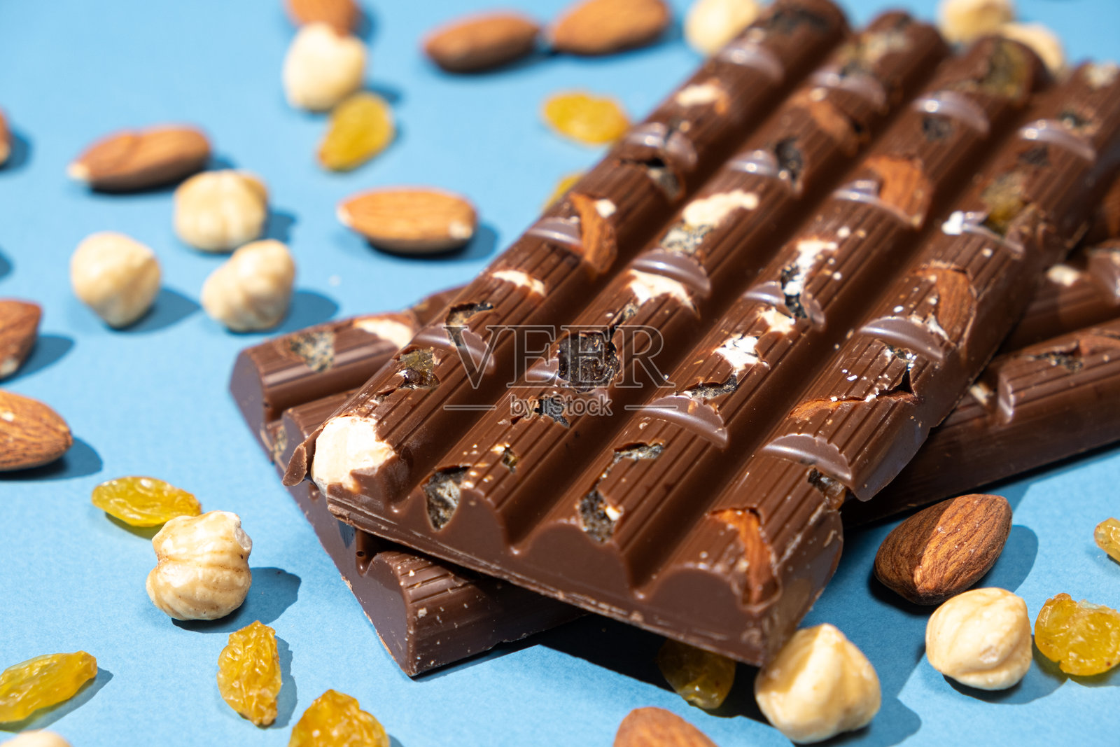 坚果巧克力棒与散落的坚果和葡萄干在蓝色背景上。照片摄影图片