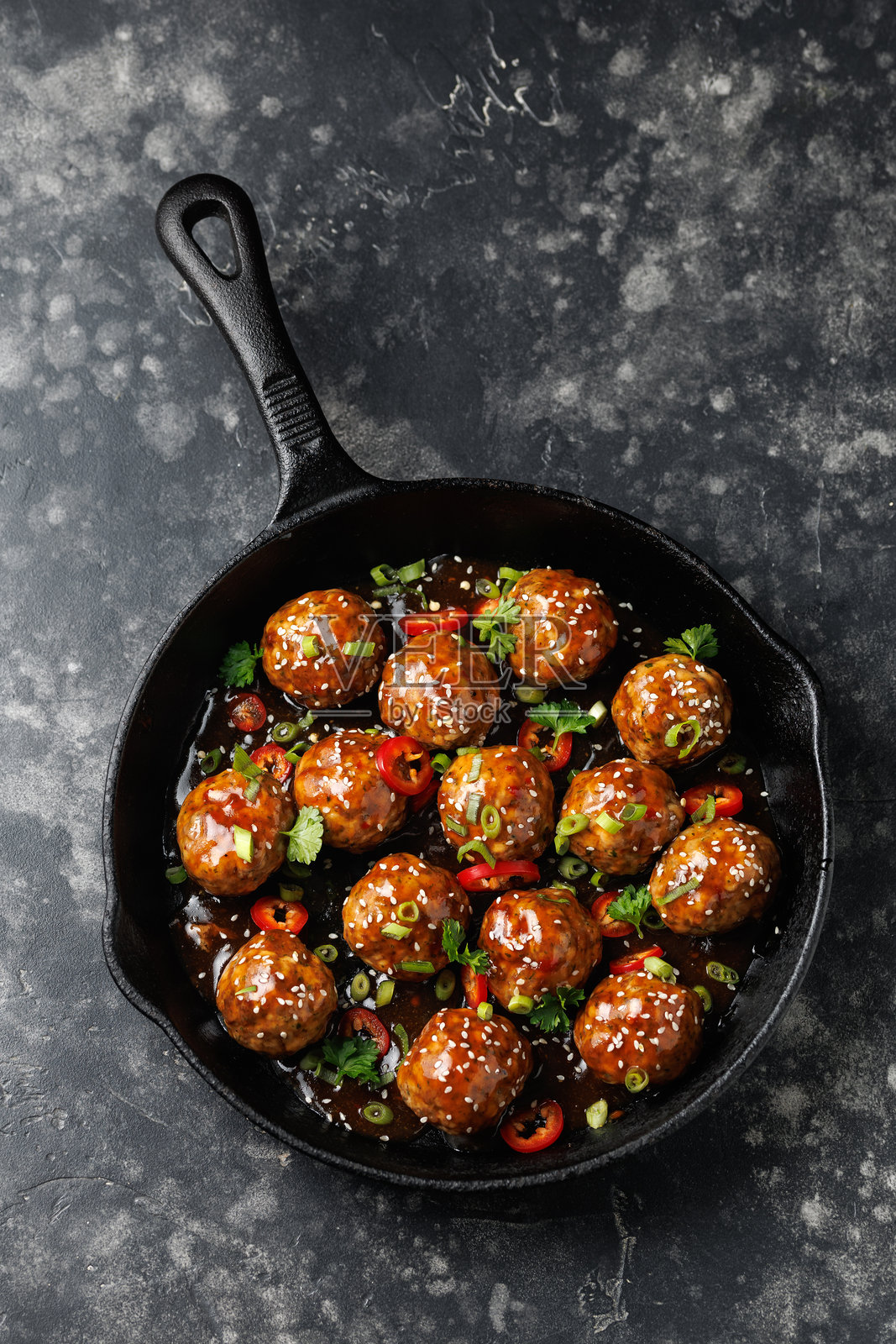 铁锅中放有牛肉丸,配以照烧酱、芝麻、辣椒和香草。照片摄影图片