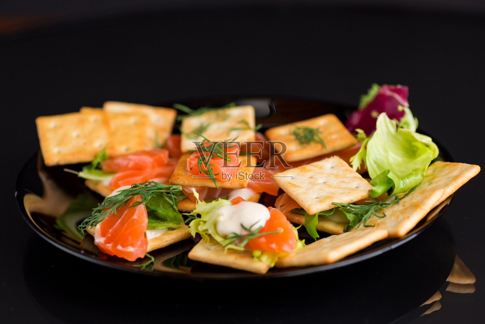 小点心开胃菜,配有饼干和轻微咸味的红鱼三文鱼,背景为黑色。照片摄影图片