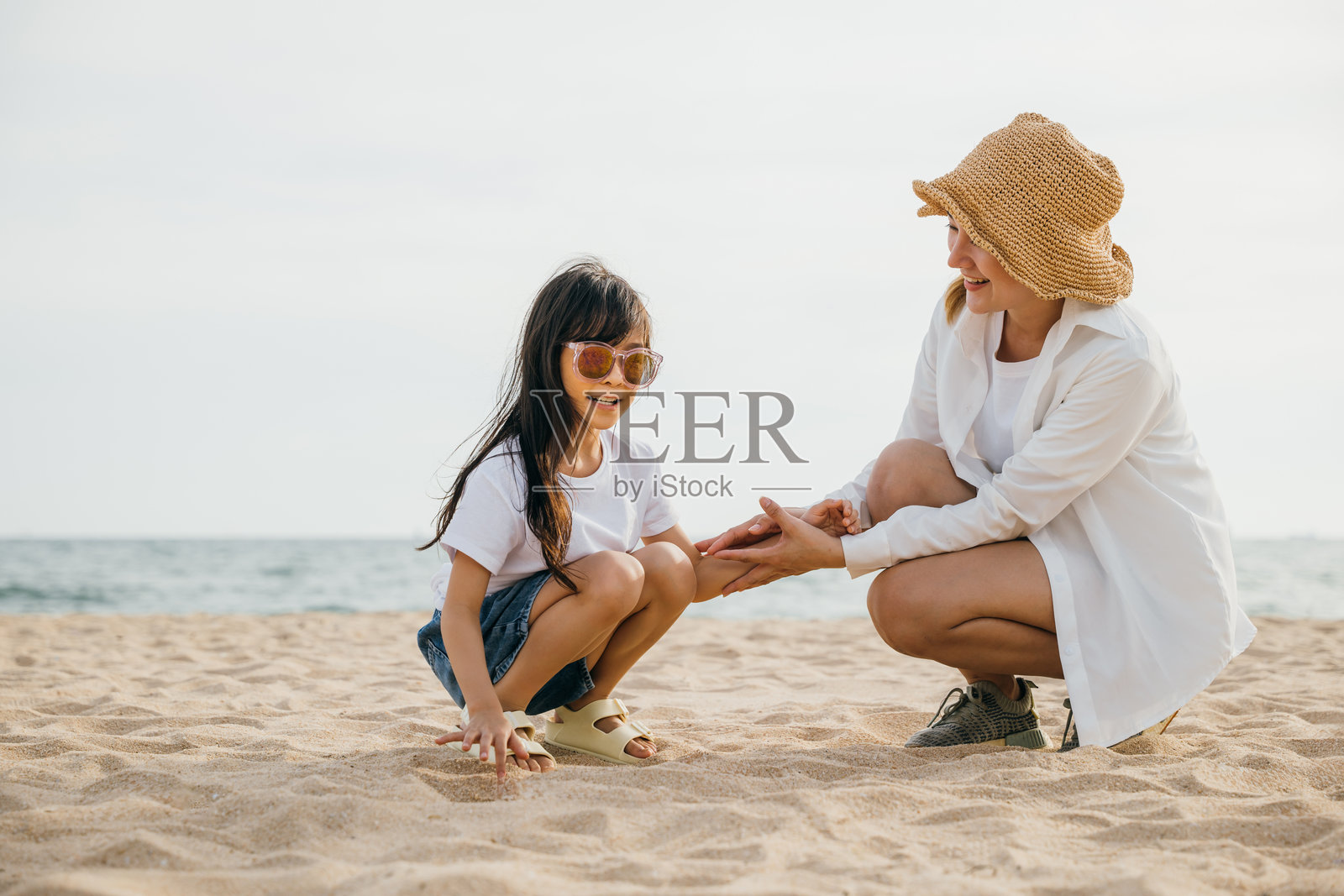 快乐的家庭在海滩度假。母亲和女儿一起坐在沙滩上玩耍。加勒比海的日落带来了欢乐、笑声和团聚。关爱、亲密和幸福在这一刻得以体现。照片摄影图片