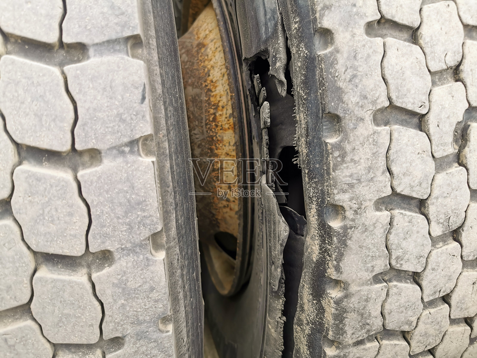 严重损坏的卡车轮胎,明显的胎面分离和大裂缝,表明磨损和潜在的爆胎风险,位于混凝土表面。照片摄影图片