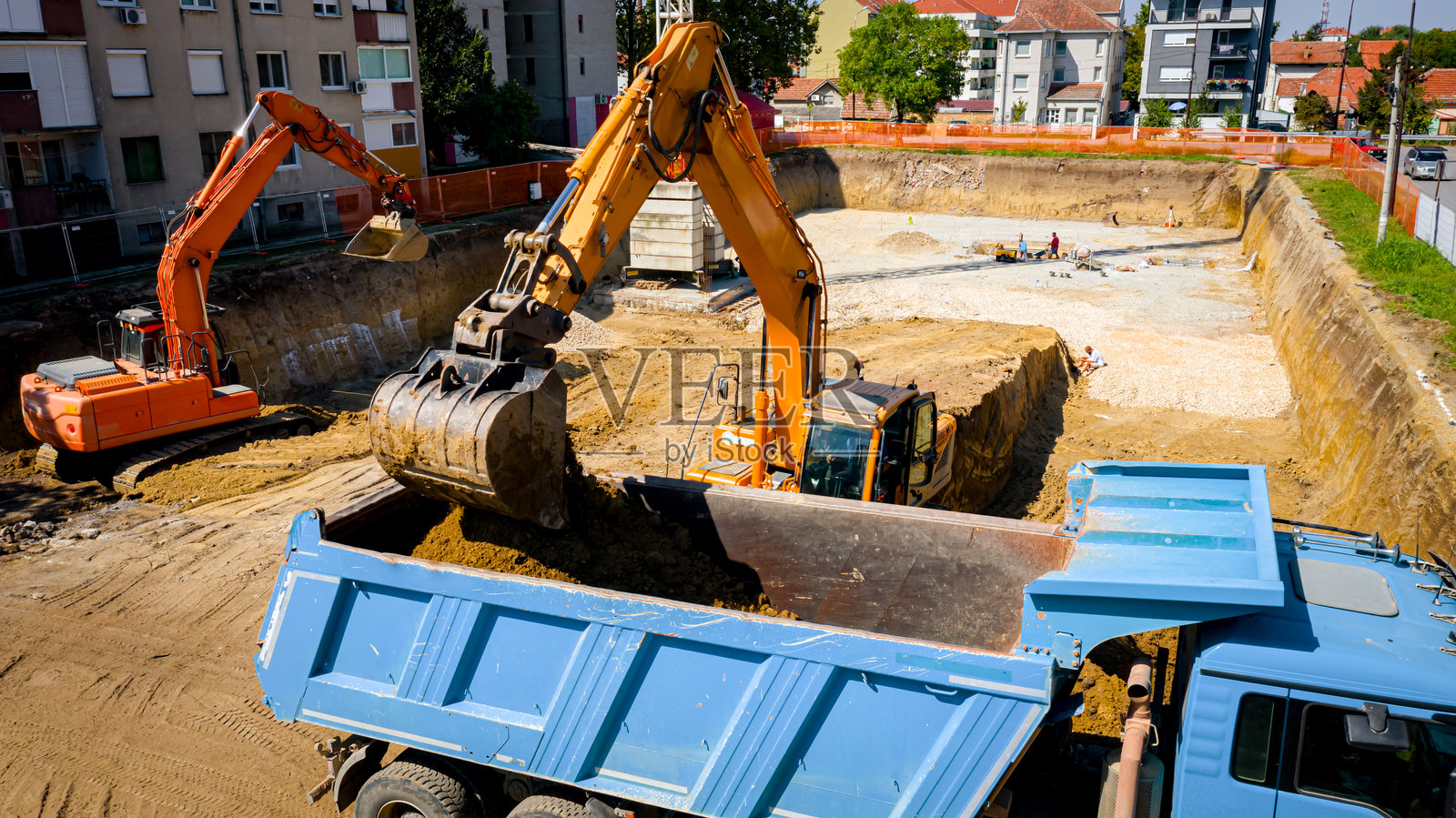 建筑工地上,俯视图显示挖掘机正在将土壤装载到卡车上。照片摄影图片