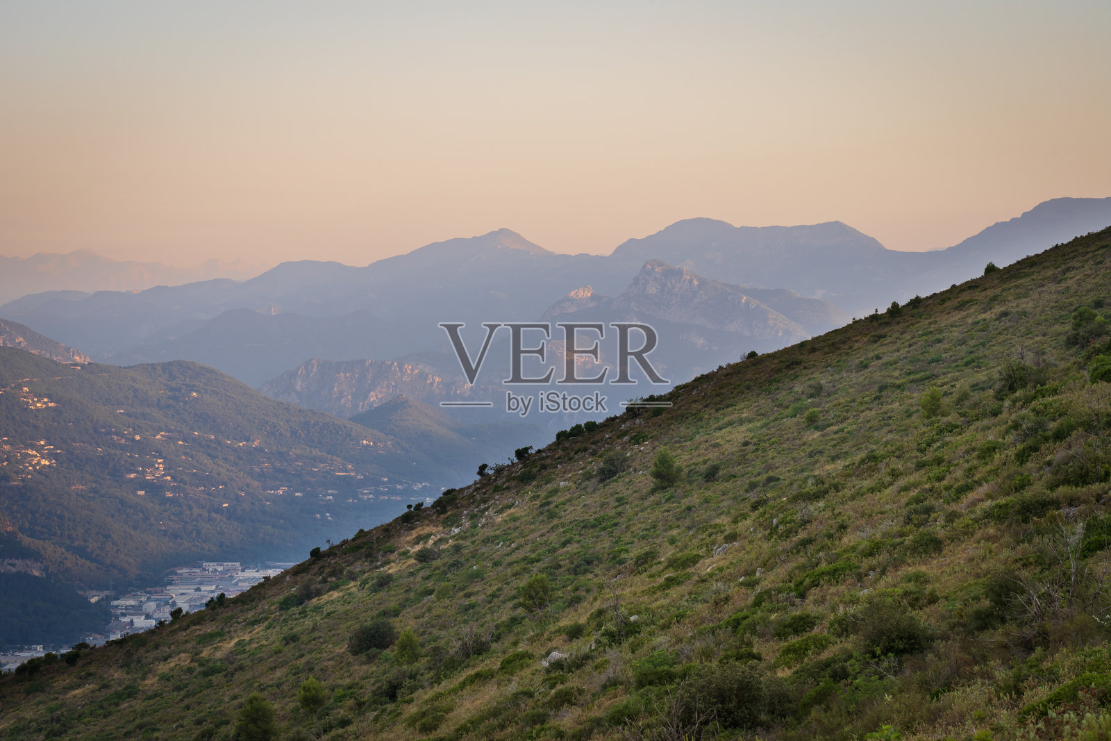法国阿尔卑斯山。日落时的山地风景。绿色坡地、树木和远处山脉的山谷景观。照片摄影图片