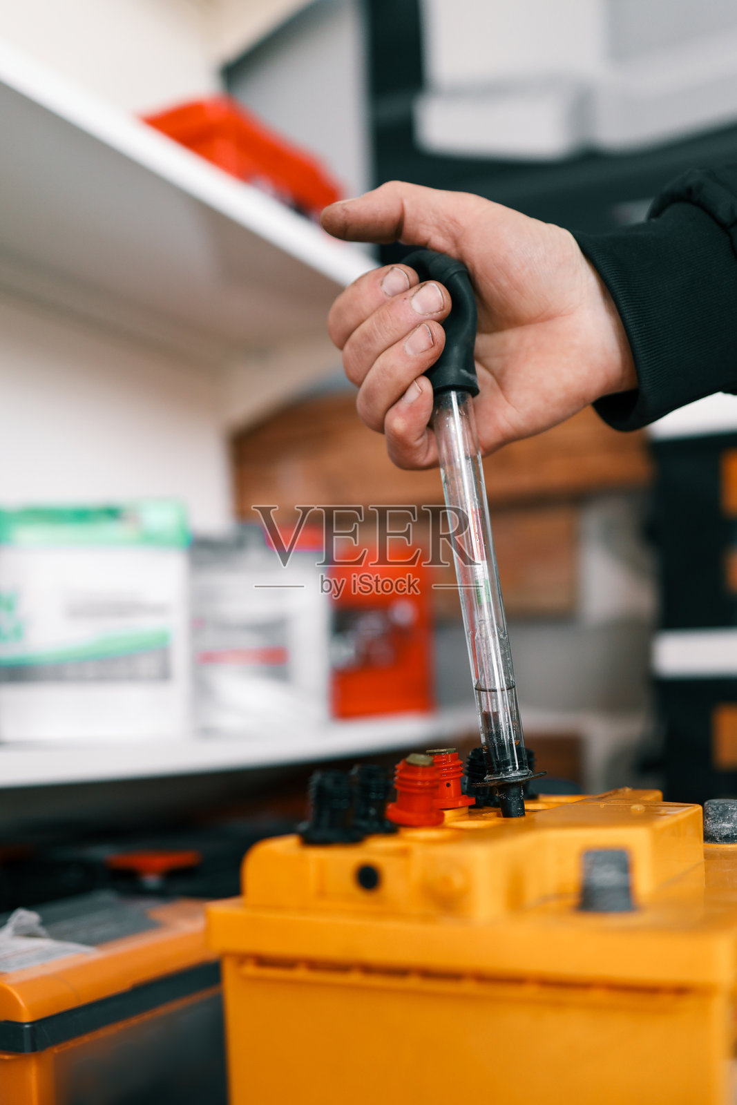 一个人正在使用比重计测试一块黄色汽车电池,电池上有明显的红色和黑色接头。用于检查电池液体密度的设备。照片摄影图片