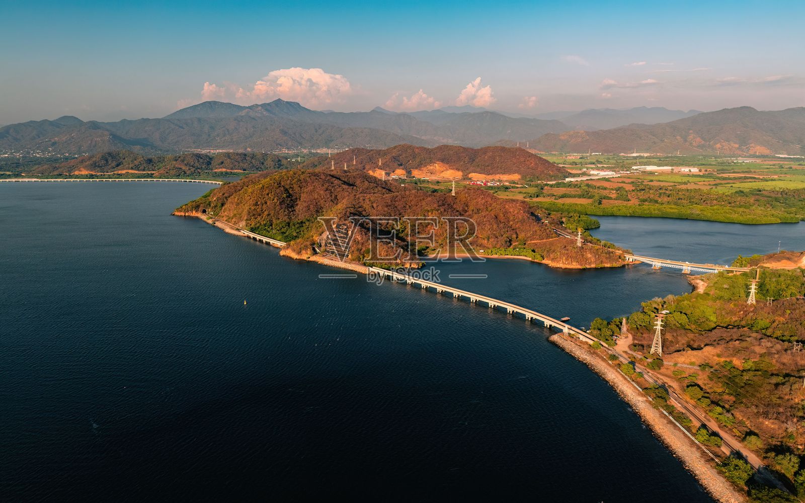 湖泊上方的风景优美的桥梁鸟瞰图,四周环绕着郁郁葱葱的山丘和山脉。照片摄影图片