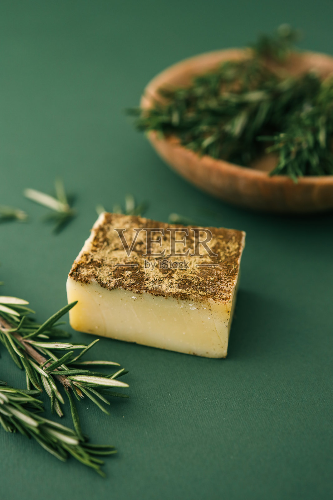 特写手工草本香皂,上面放着干迷迭香,背景为绿色纹理,旁边是装有新鲜迷迭香枝的木碗。非常适合自然和环保的概念。照片摄影图片