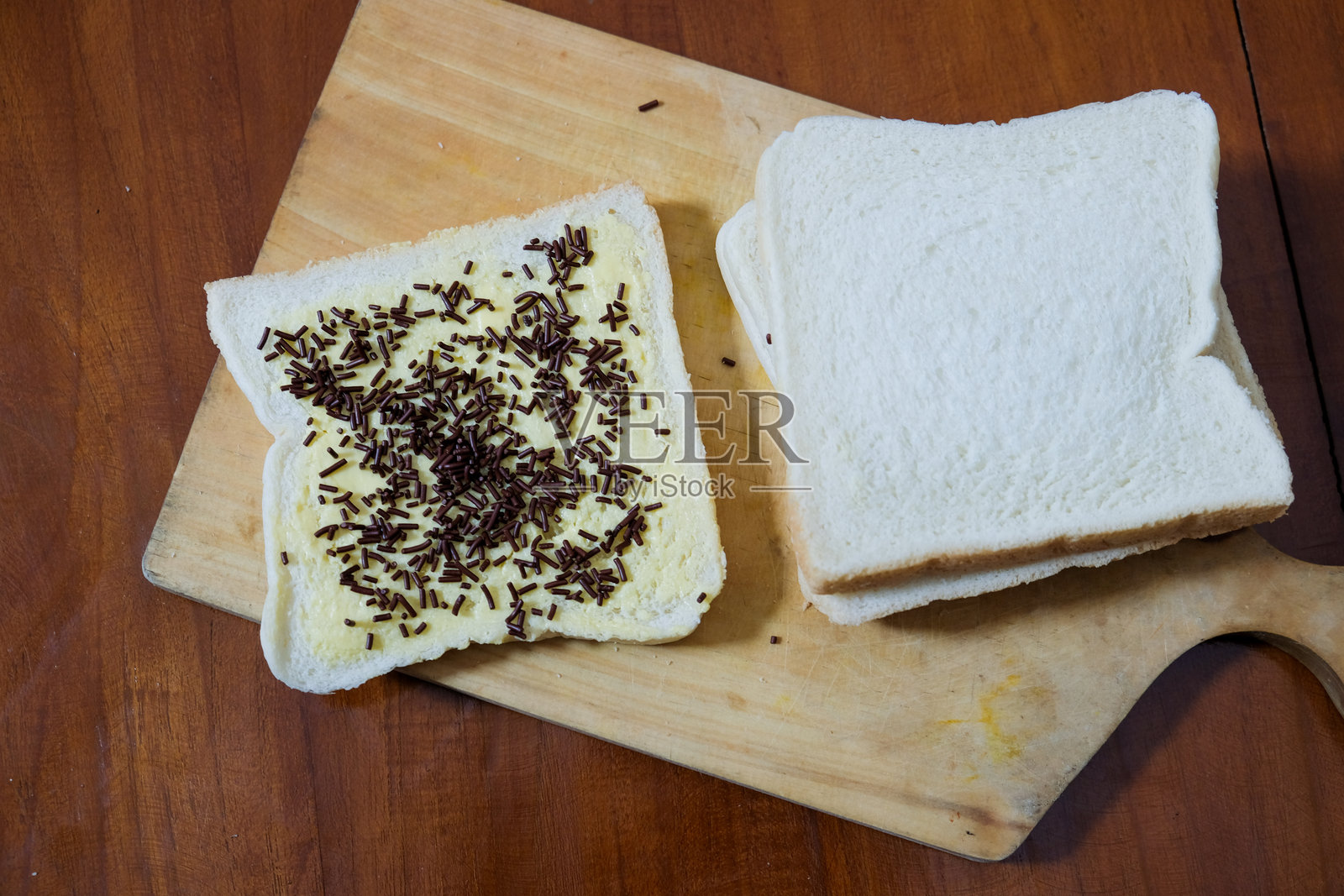 早餐用黄油涂抹的三明治面包,上面撒有巧克力糖屑,放在木质切菜板上,背景是木桌。照片摄影图片