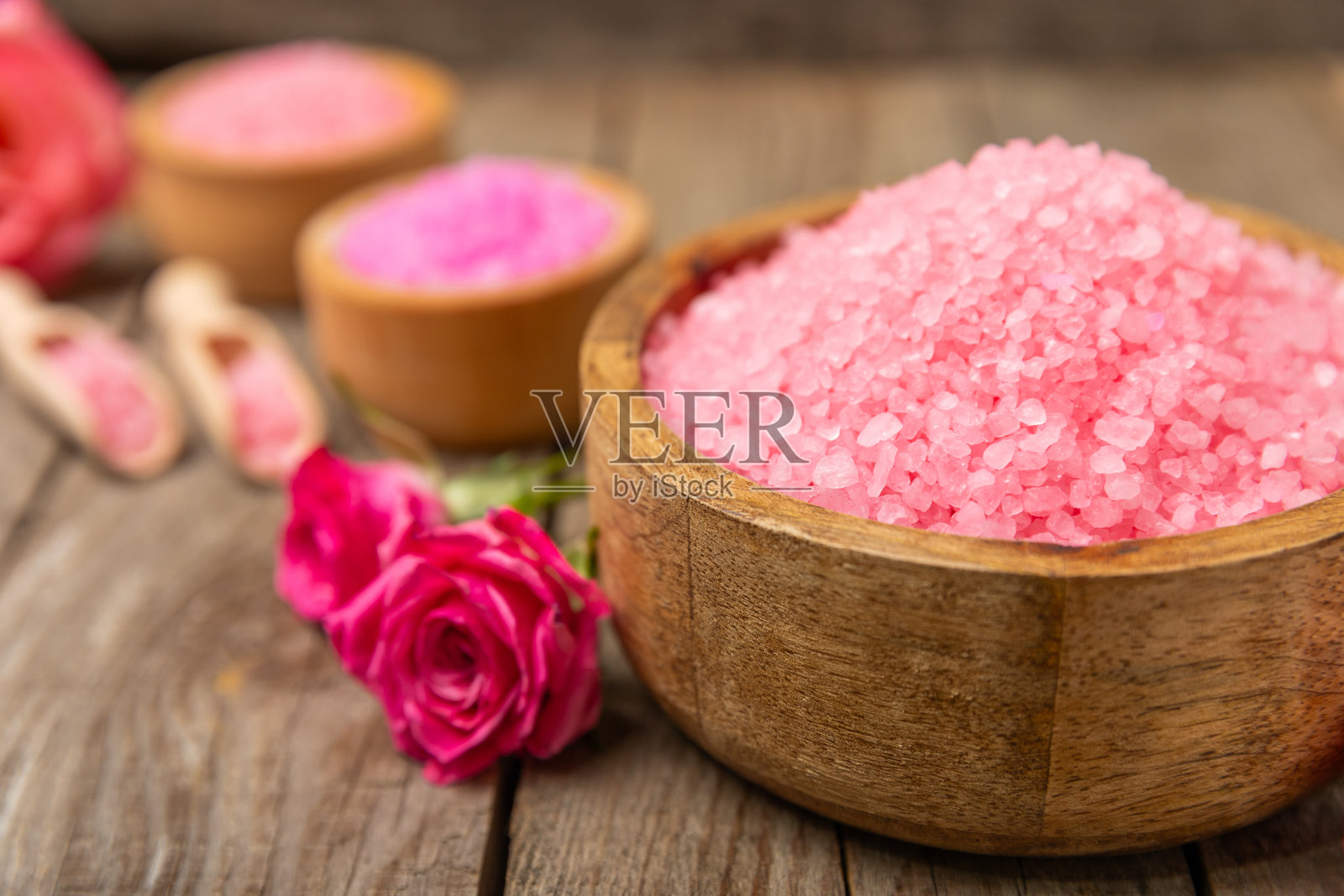 带有香气和玫瑰花的海盐浴,背景为纹理木材。粉色海盐。水疗护理。含草药和精油的天然盐。护肤概念。文本的中间留白。照片摄影图片