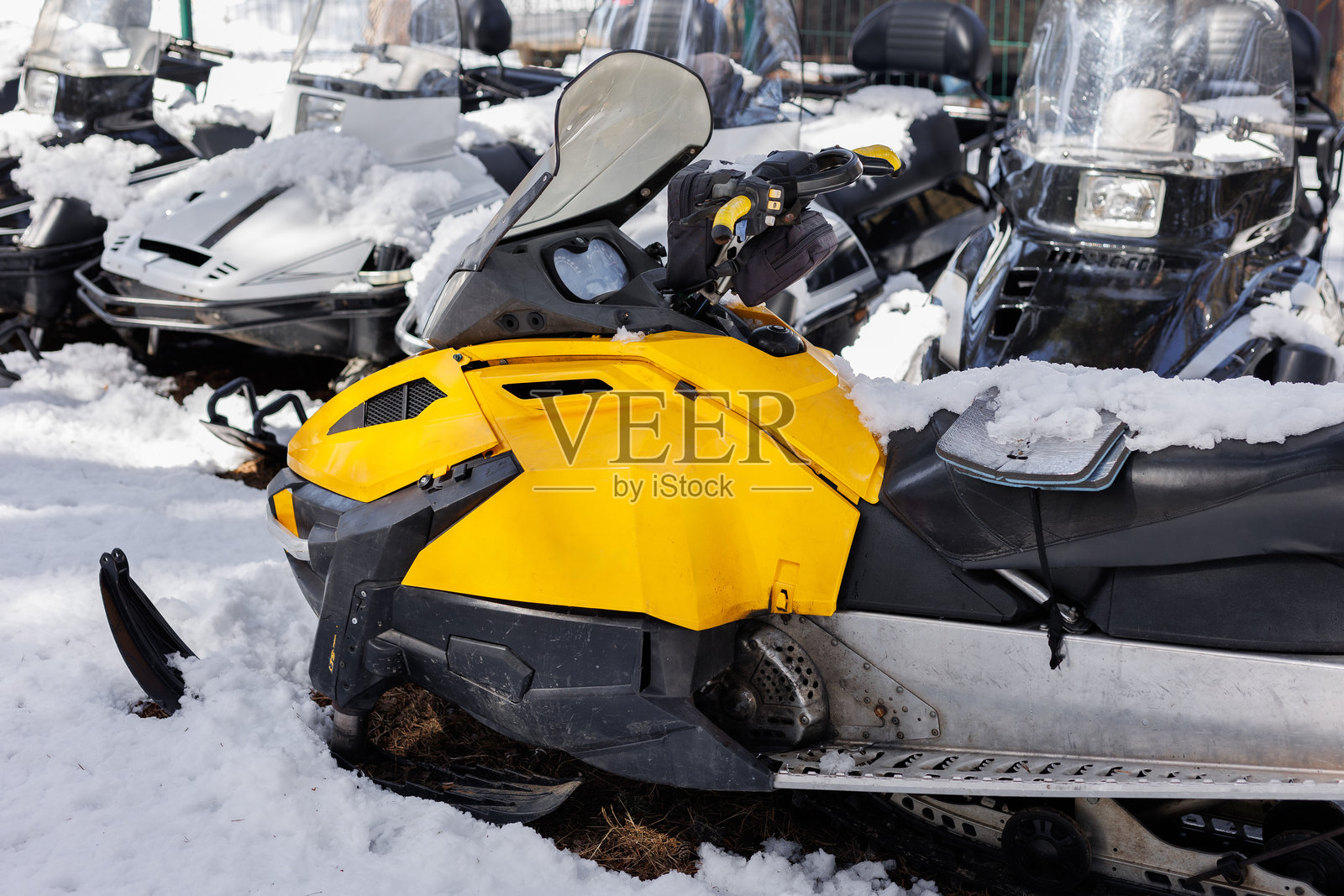 一排雪地摩托停在滑雪度假村山坡上森林边缘的雪地上。照片摄影图片