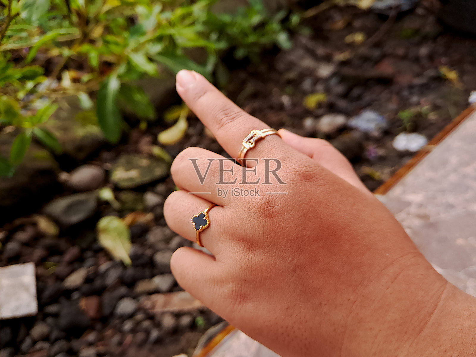 手上佩戴着精致的金手链和戒指,背景是郁郁葱葱的绿叶。非常适合珠宝摄影和时尚配饰。照片摄影图片