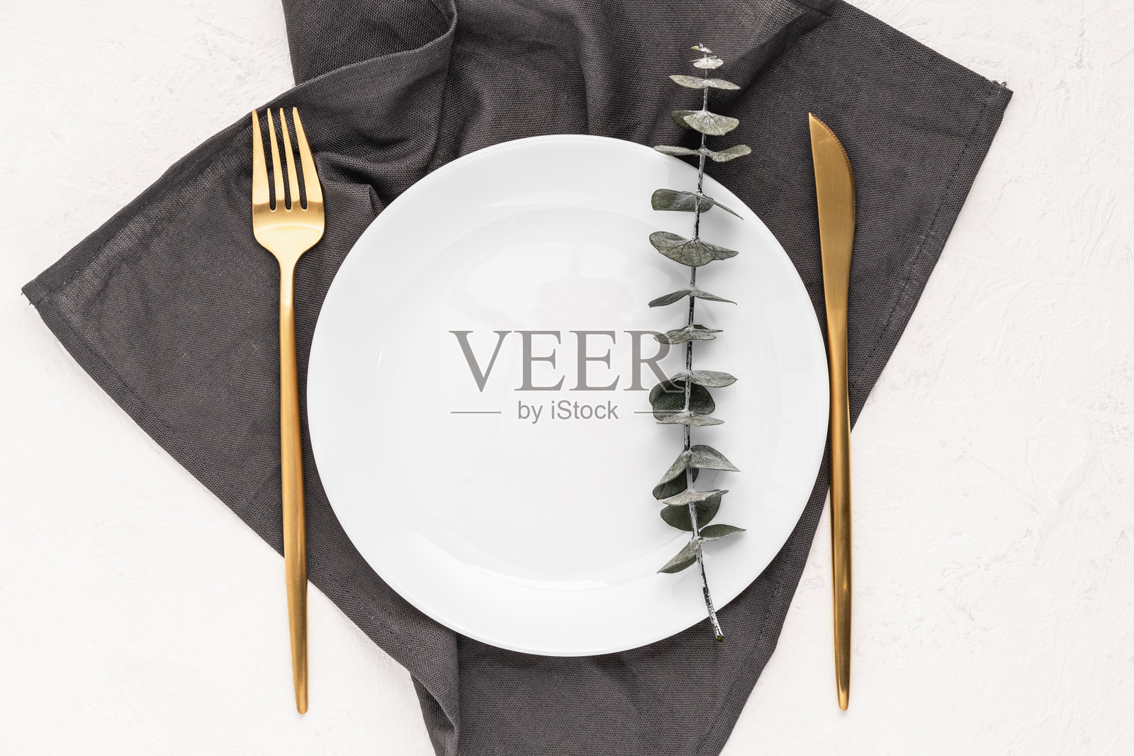 灰色餐巾上的白色盘子和餐具,搭配桉树枝。问候卡、邀请函、菜单卡的样板。照片摄影图片